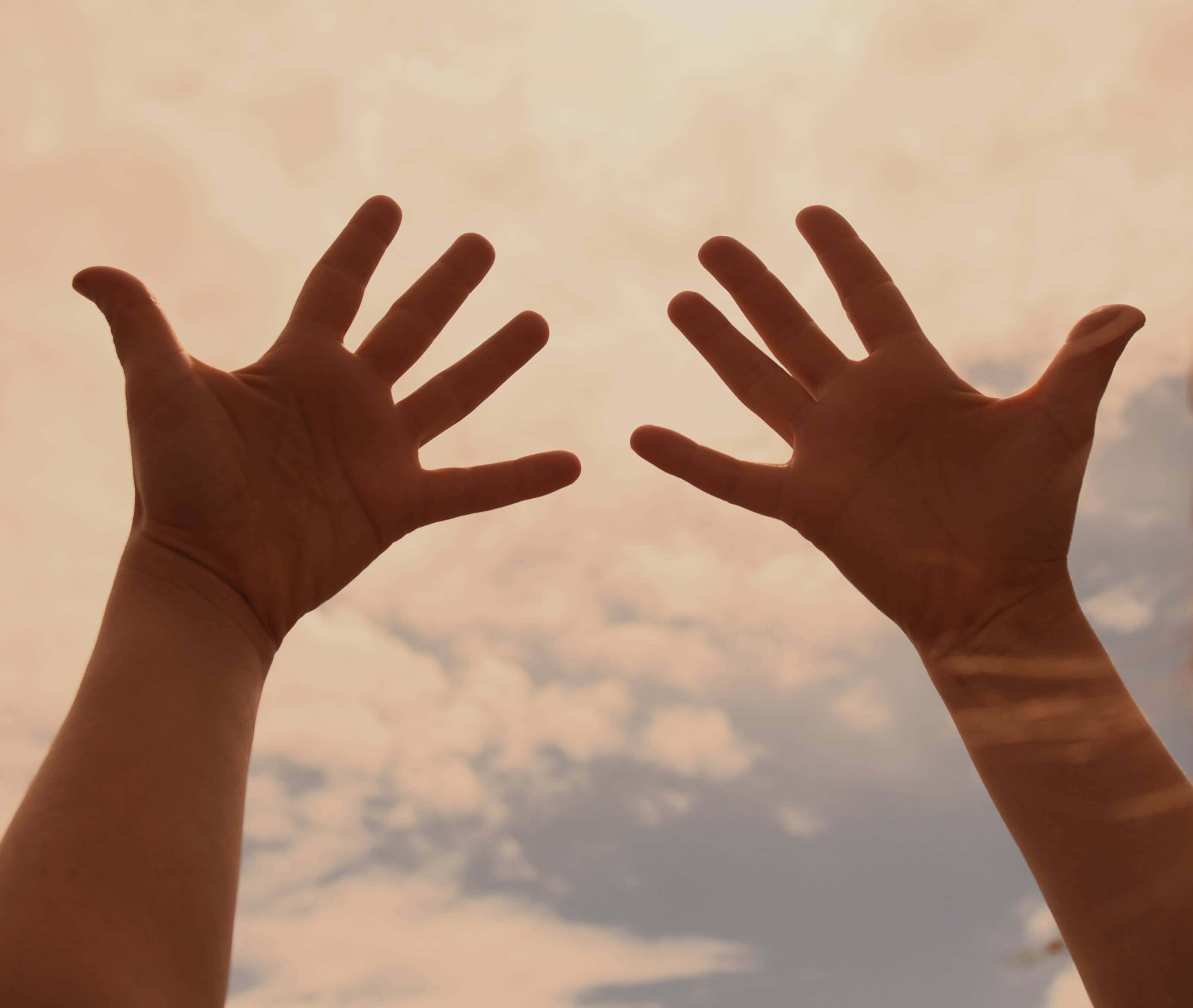 hands up 桌布 壁紙 — 兩隻張開的手向上伸展，襯著日落時分柔和的金色天空和散落的雲朵。