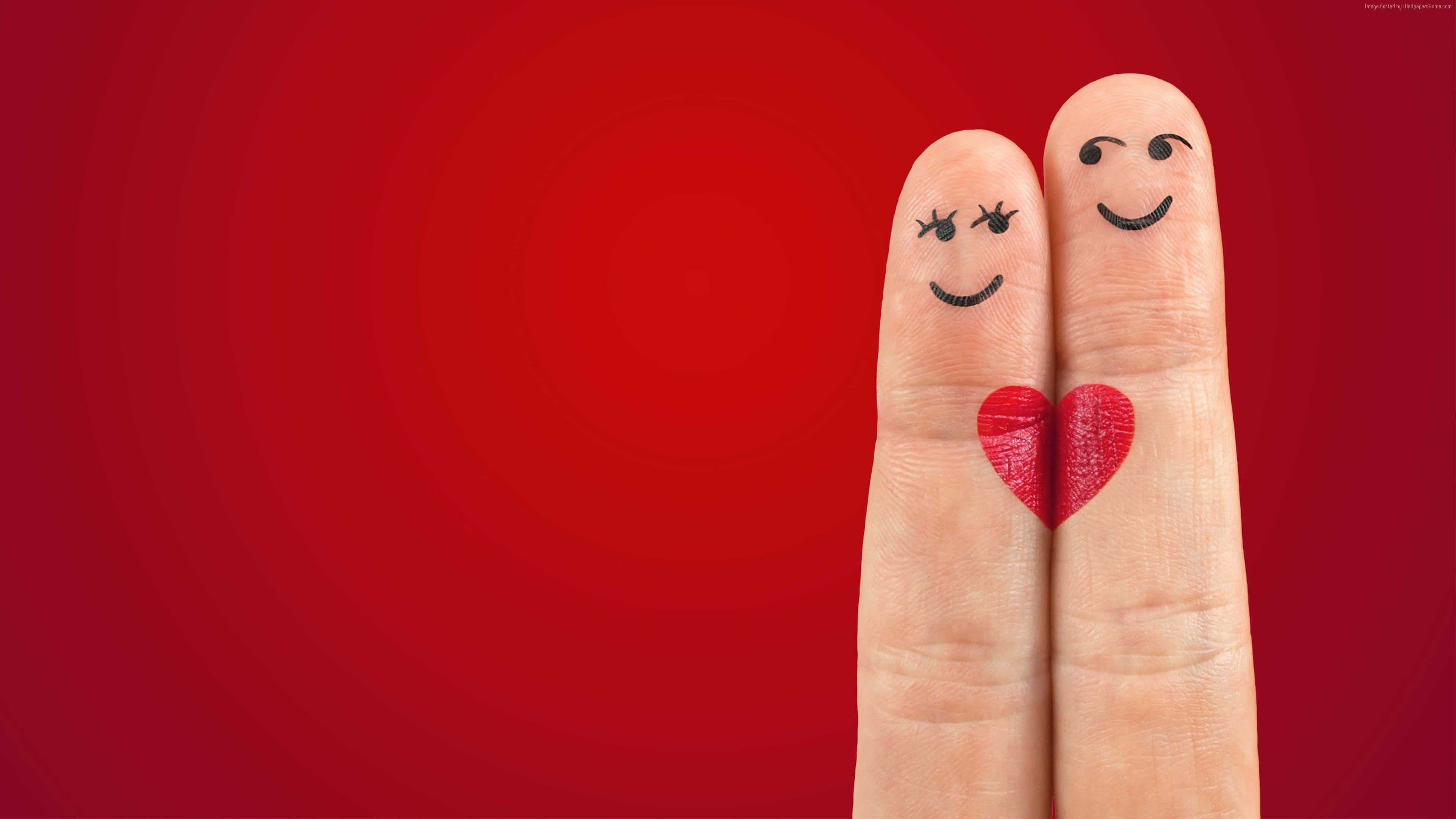 4K Love 桌布 壁紙 — 兩隻微笑的手指，帶有繪製的臉孔，它們之間有一顆心，背景是充滿活力的紅色漸變。
