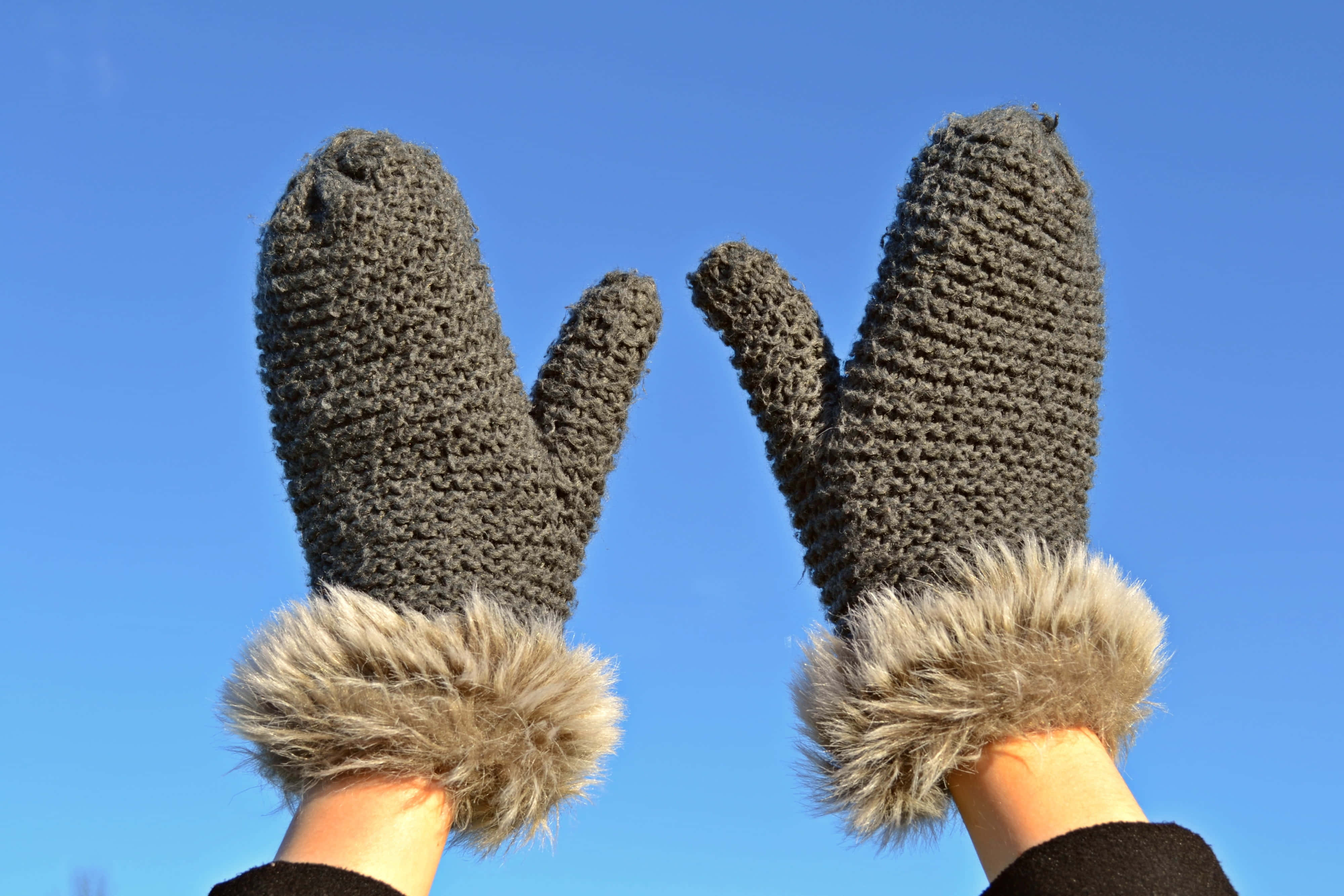 Mittens 桌布 壁紙 — 兩隻戴著灰色針織連指手套、帶有毛絨袖口的手，在清澈的藍天下舉起。