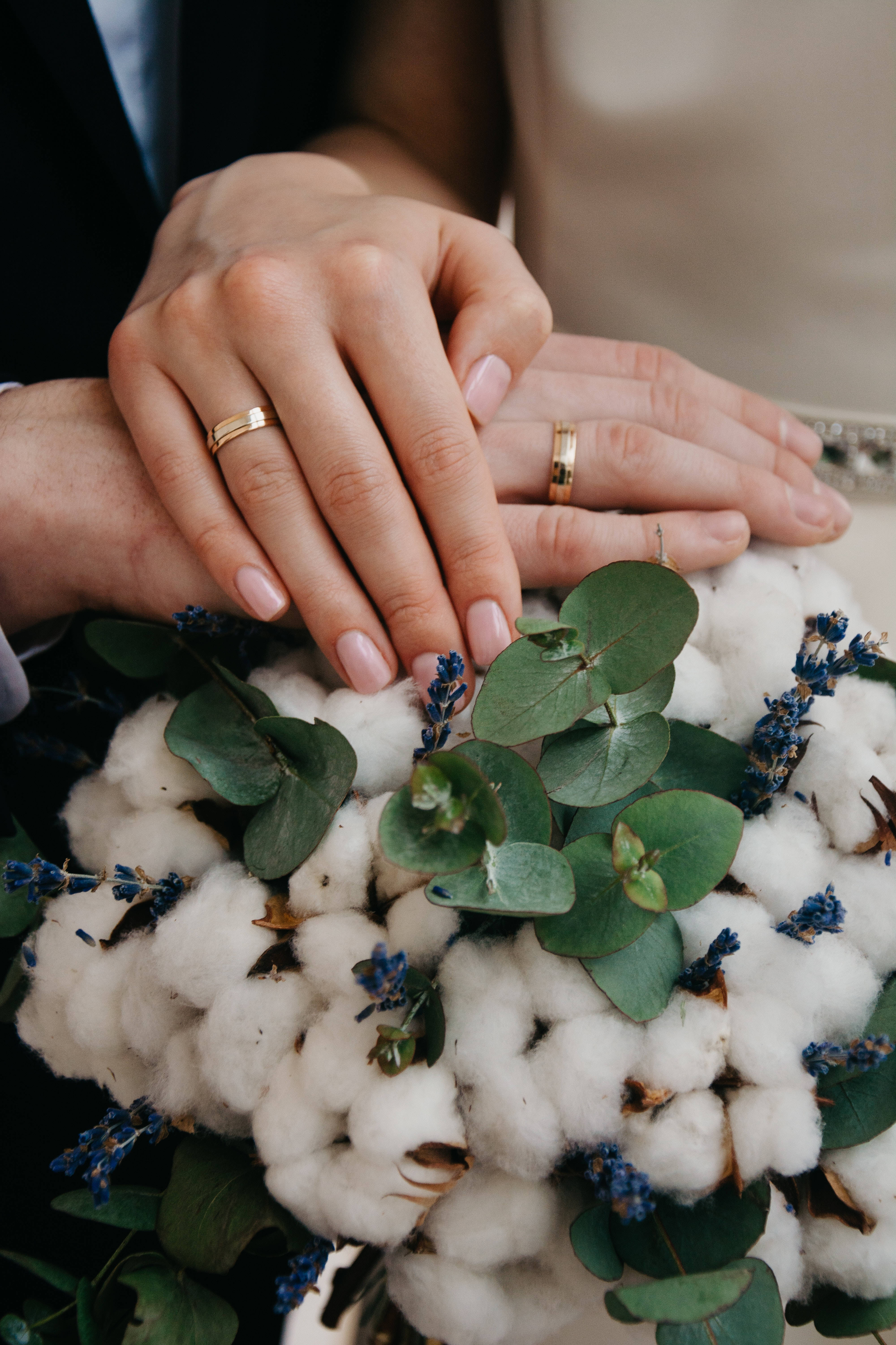 浪漫愛情 桌布 壁紙 — 兩隻戴著結婚戒指的手輕輕地放在一個柔軟的棉花花束上，花束點綴著綠色桉樹和小藍花。