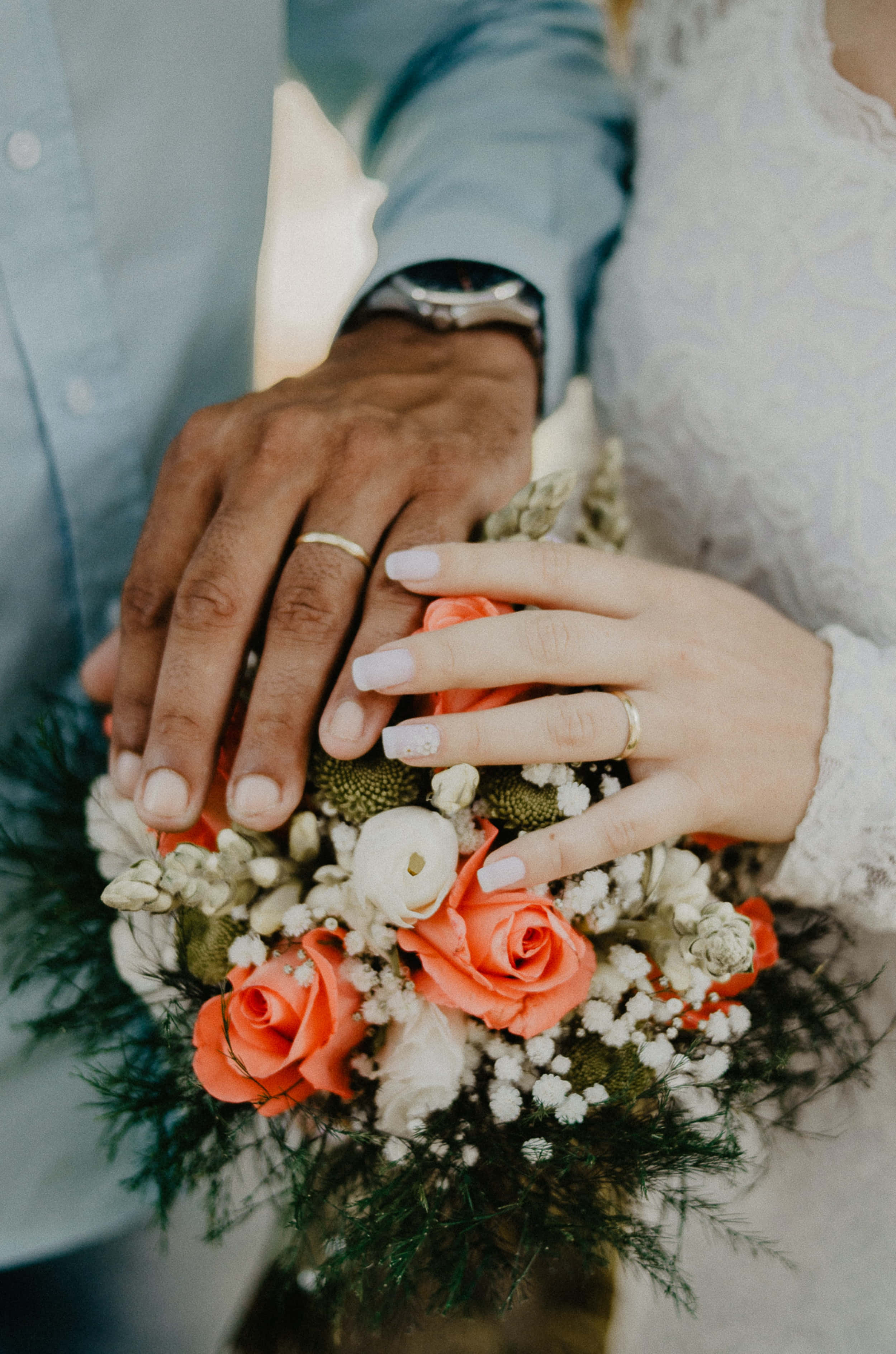 Wedding Bouquet 桌布 壁紙 — 兩隻戴著結婚戒指的手輕輕放在一束珊瑚玫瑰和白色滿天星花束上。