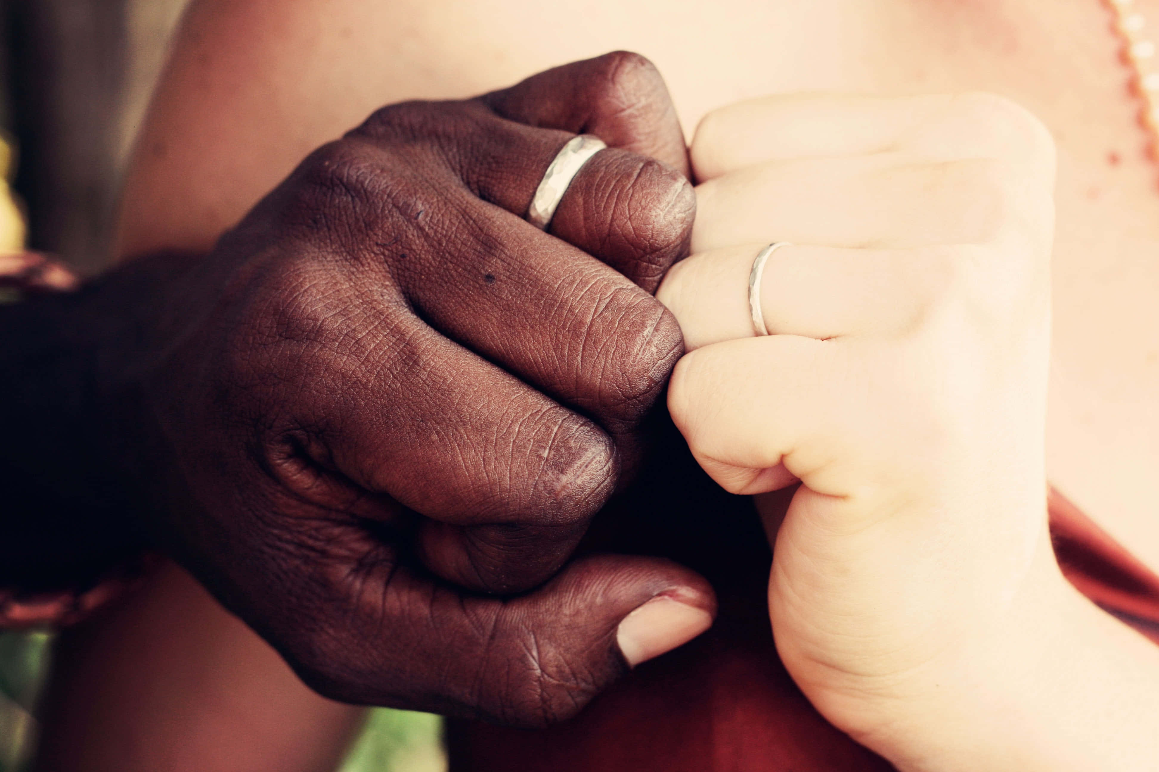 Interracial 桌布 壁紙 — 兩隻手，一深一淺，戴著結婚戒指，在溫暖柔和焦點中緊握在一起。