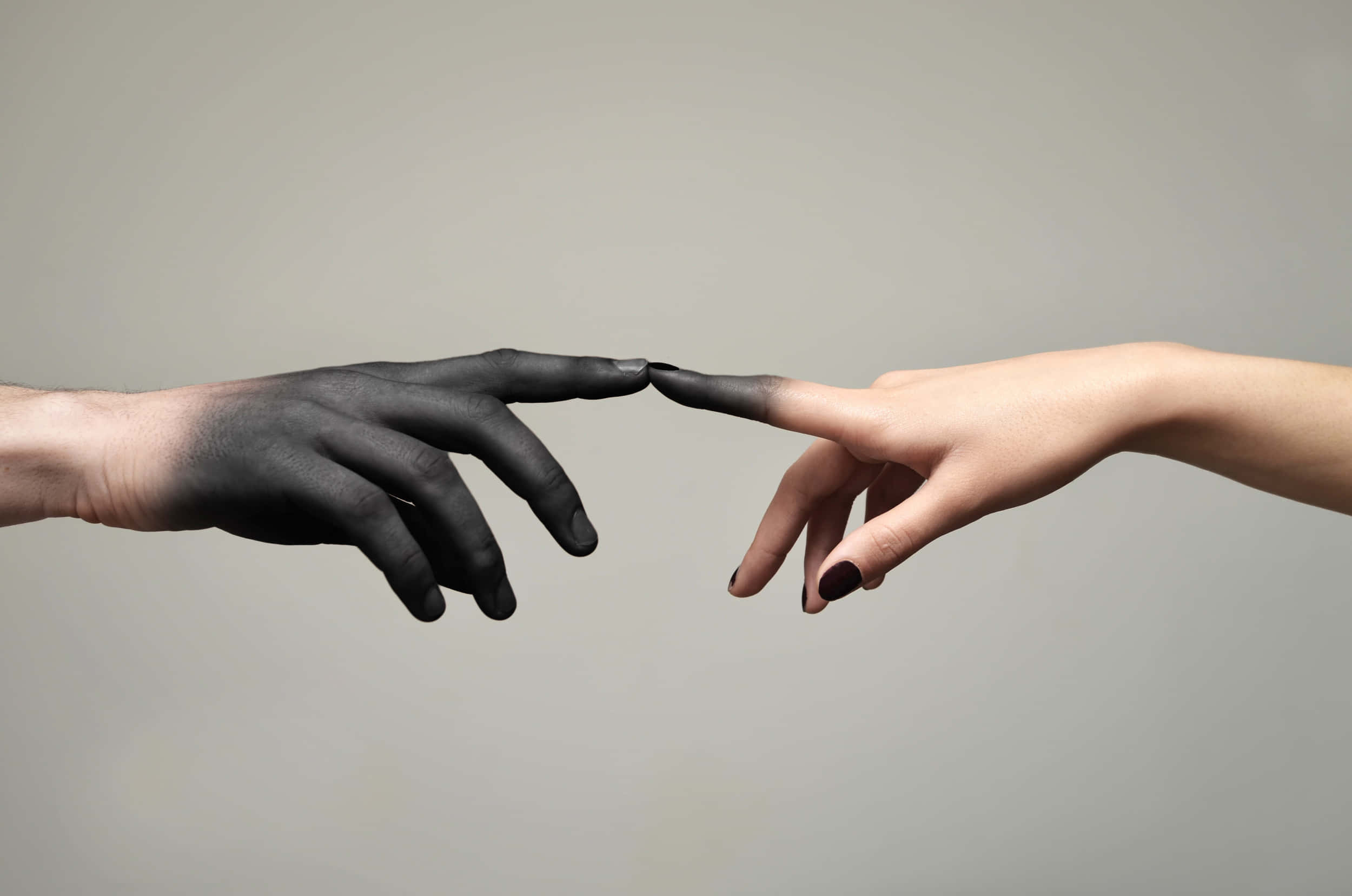 hands 桌布 壁紙 — 兩隻手，一隻深色和一隻淺色，越過中性背景伸出，指尖幾乎相觸，象徵著聯繫的姿態。