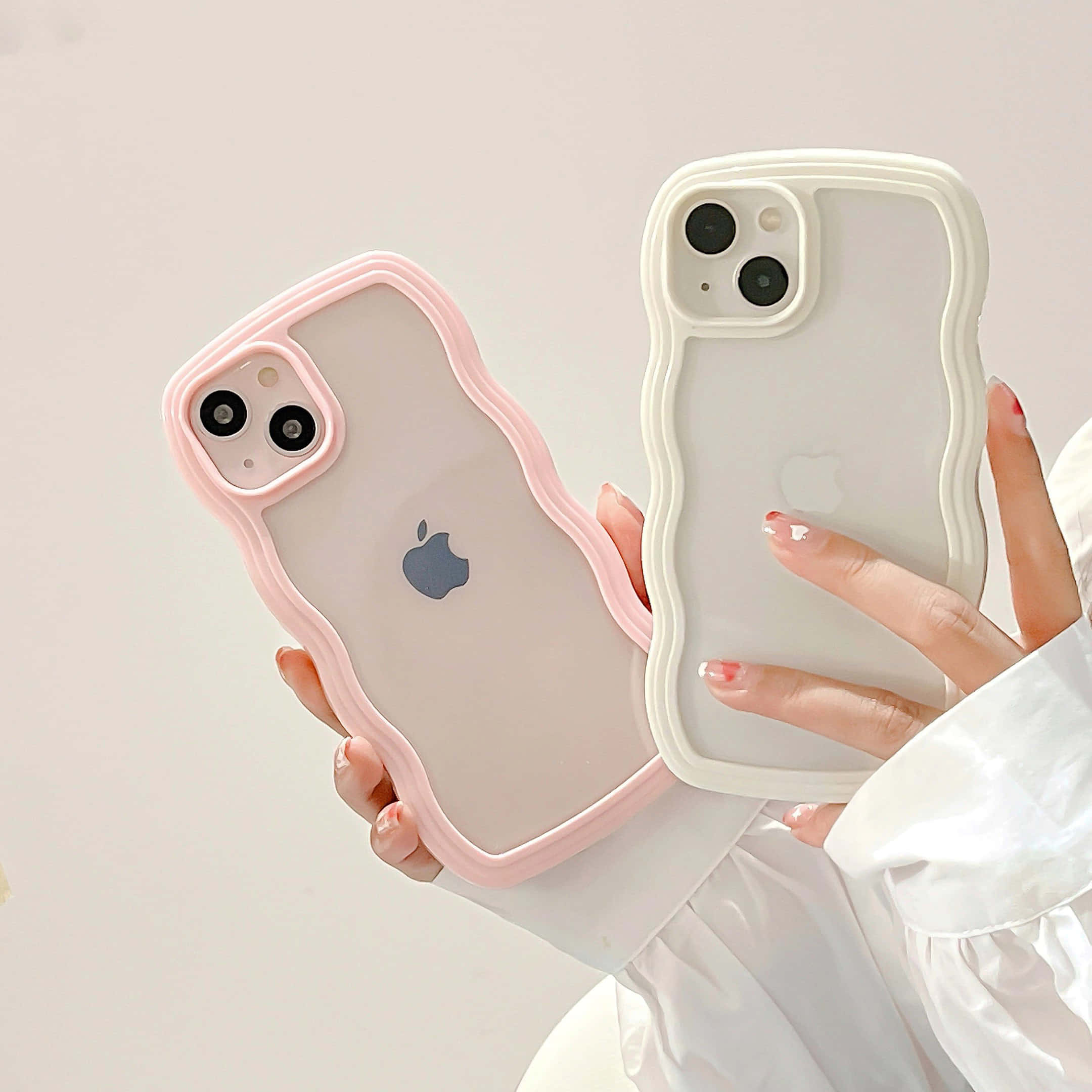 iPhone 美學 桌布 壁紙 — 兩隻手分別拿著時尚波浪邊手機殼，一個粉紅色一個白色，背景是柔和的中性色調。