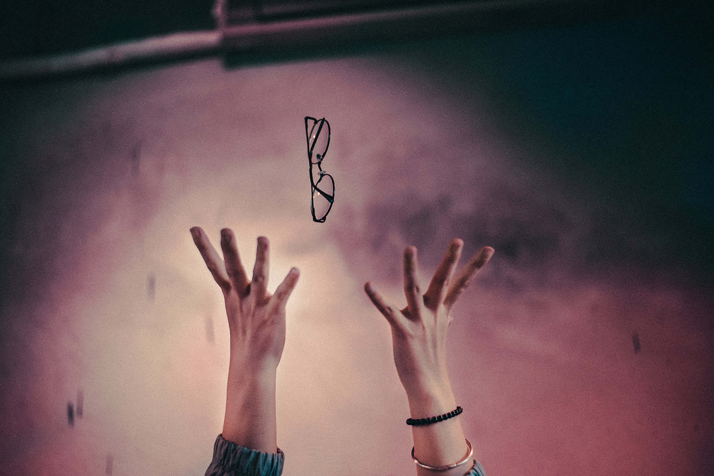 hands 桌布 壁紙 — 兩隻手向上伸向一對漂浮的眼鏡，背景是朦朧的粉紅色和紫色。