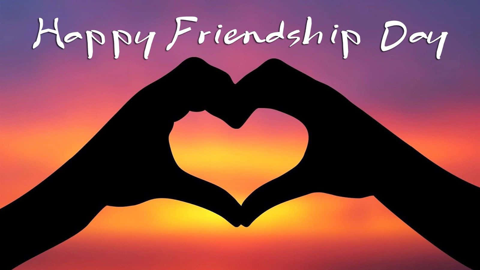 Friendship Day 桌布 壁紙 — 兩隻手在充滿活力的日落天空下形成心形，並帶有「Happy Friendship Day」文字。