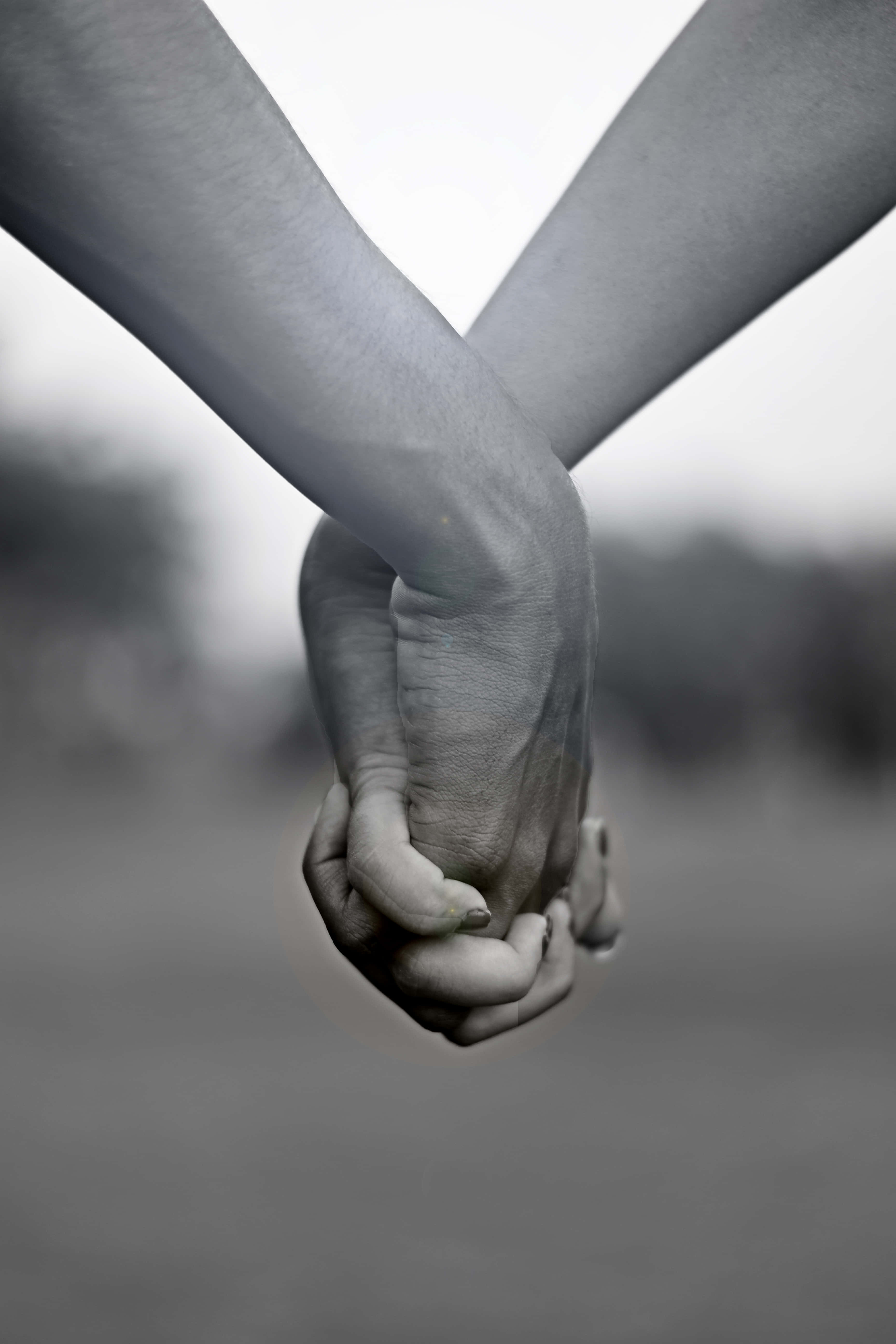 Holding Hands 桌布 壁紙 — 兩隻手在單色特寫中緊緊相握，背景是模糊的戶外景色。