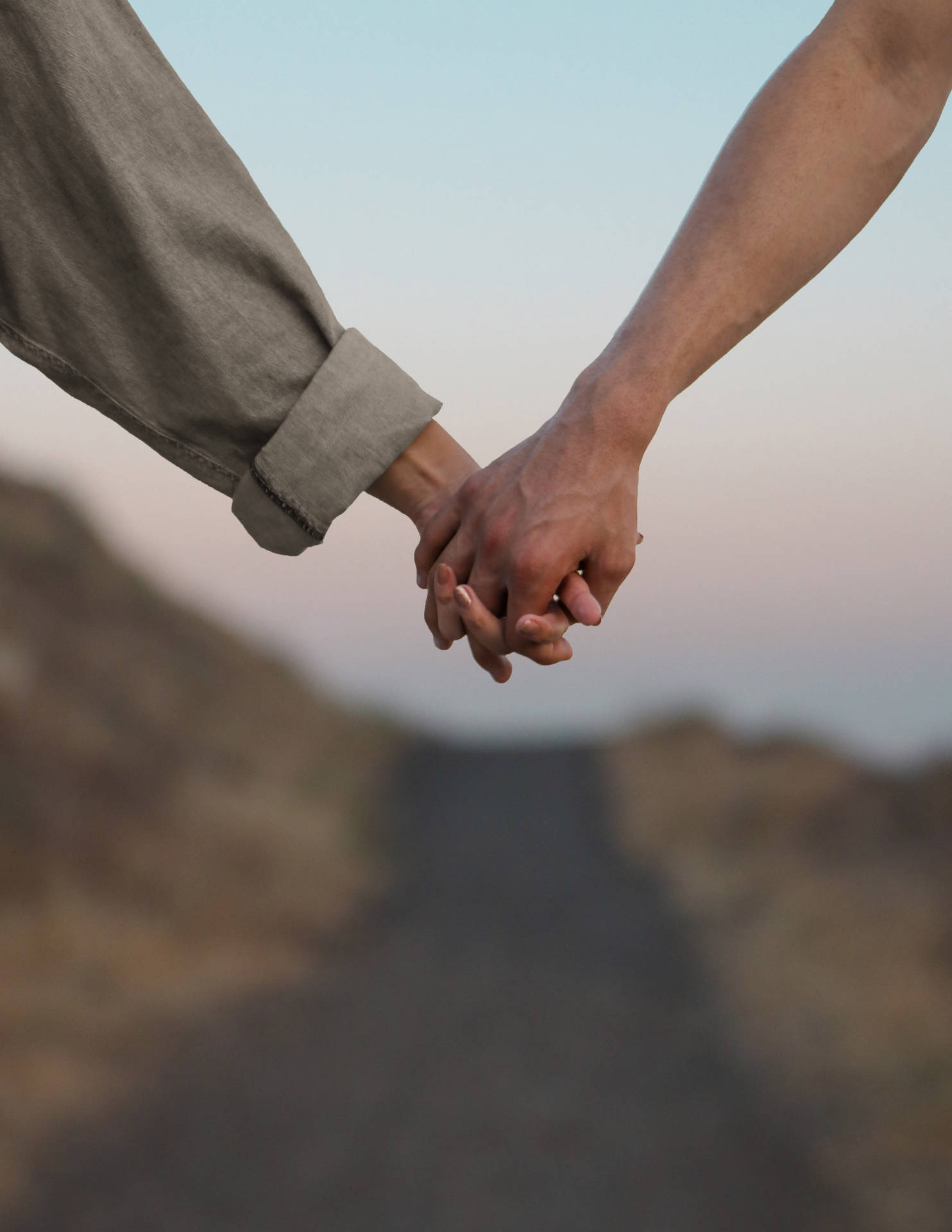 hands 桌布 壁紙 — 兩隻手在日落時分緊緊相握於蜿蜒的山路上，天空呈現柔和粉彩。