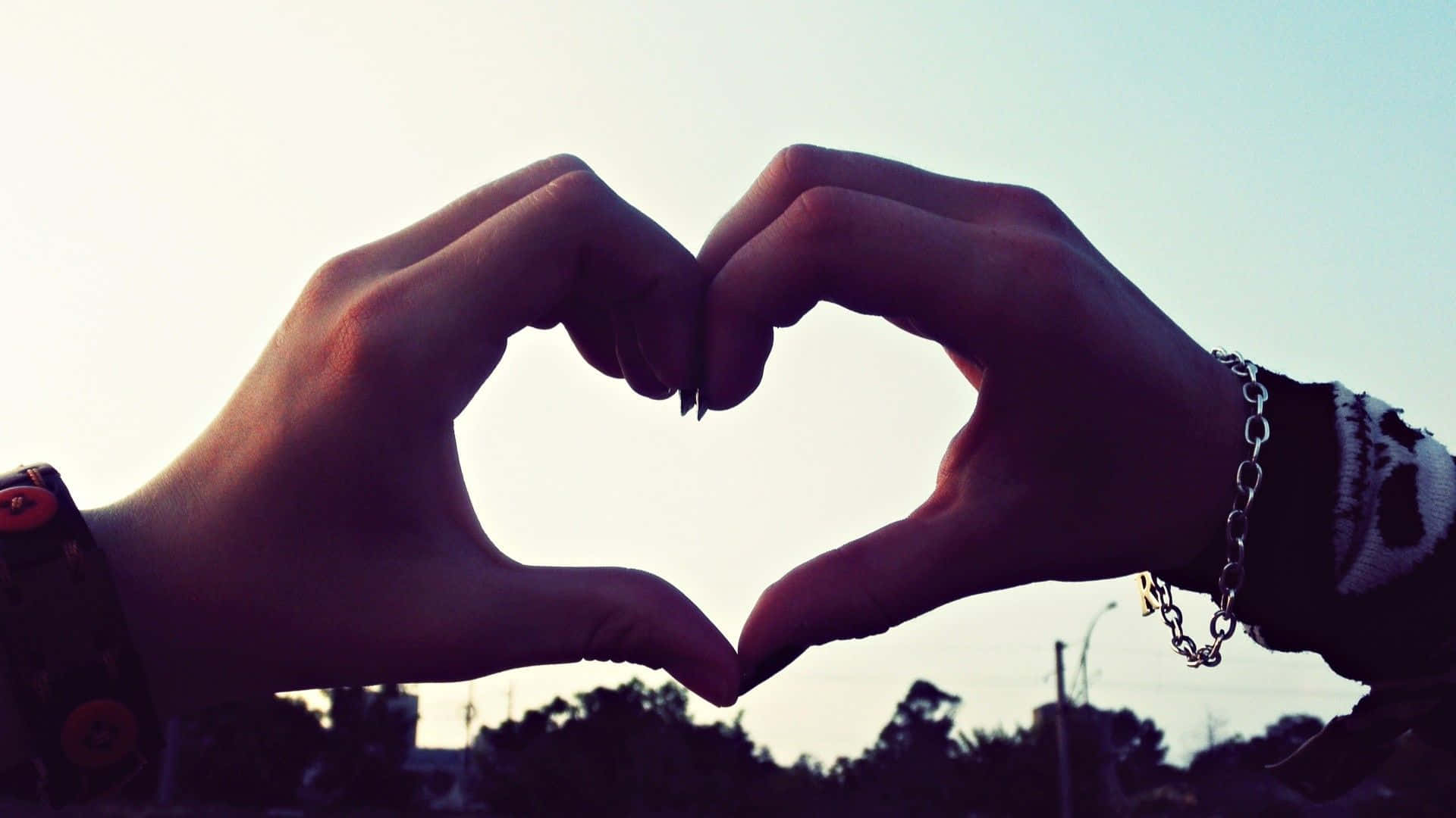 Heart Shape 桌布 壁紙 — 兩隻手在柔和的暮色天空下，襯著剪影樹木和城市背景，形成一個心形。