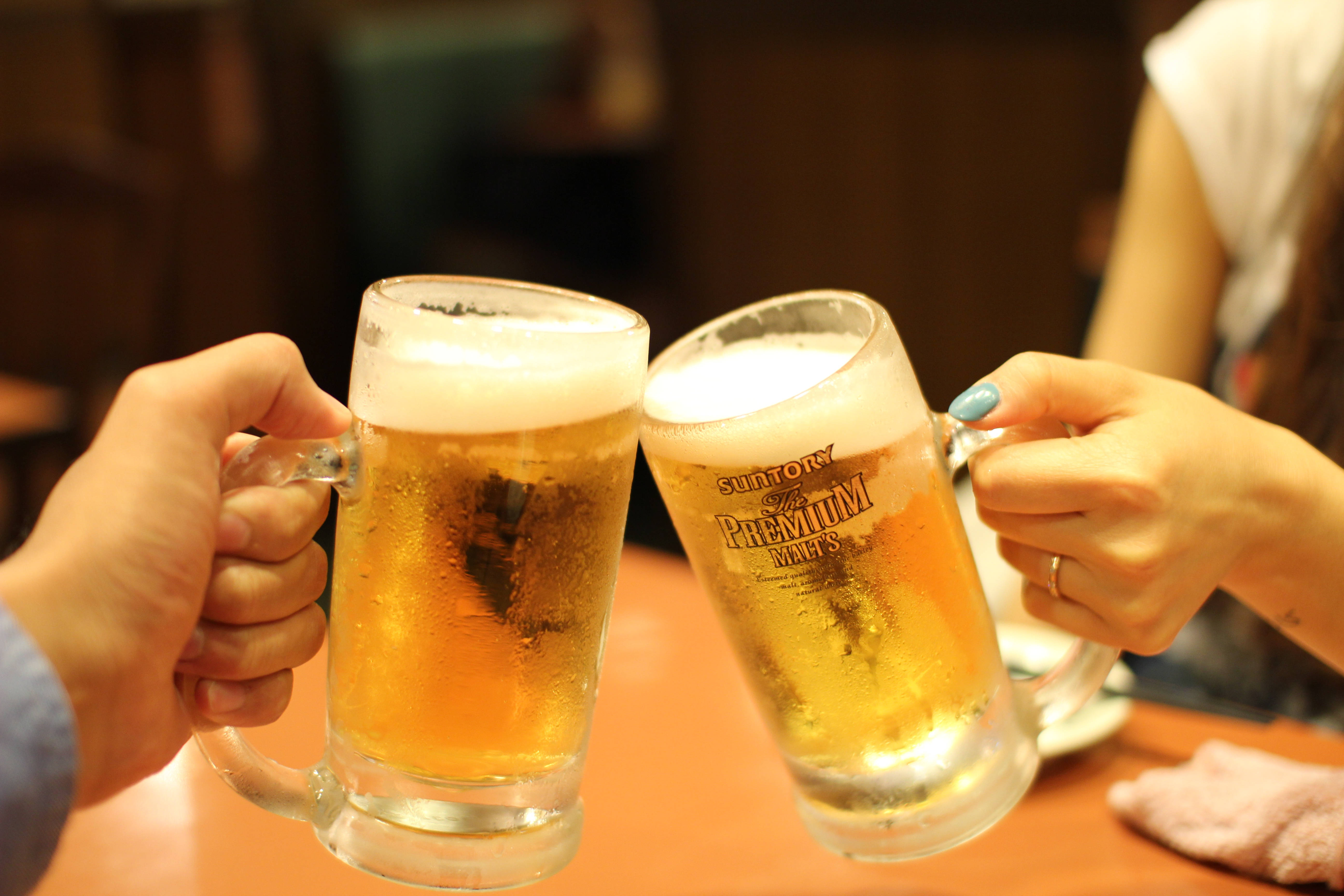 Cheers 桌布 壁紙 — 兩隻手在溫暖的室內環境中碰杯，冰凍的啤酒杯裝滿了金色啤酒和白色泡沫。