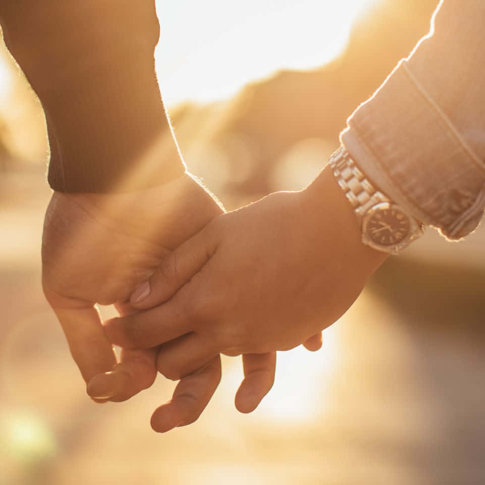 Holding Hands 桌布 壁紙 — 兩隻手在溫暖的金色日落光芒中緊握，帶有柔和鏡頭光暈和模糊背景。
