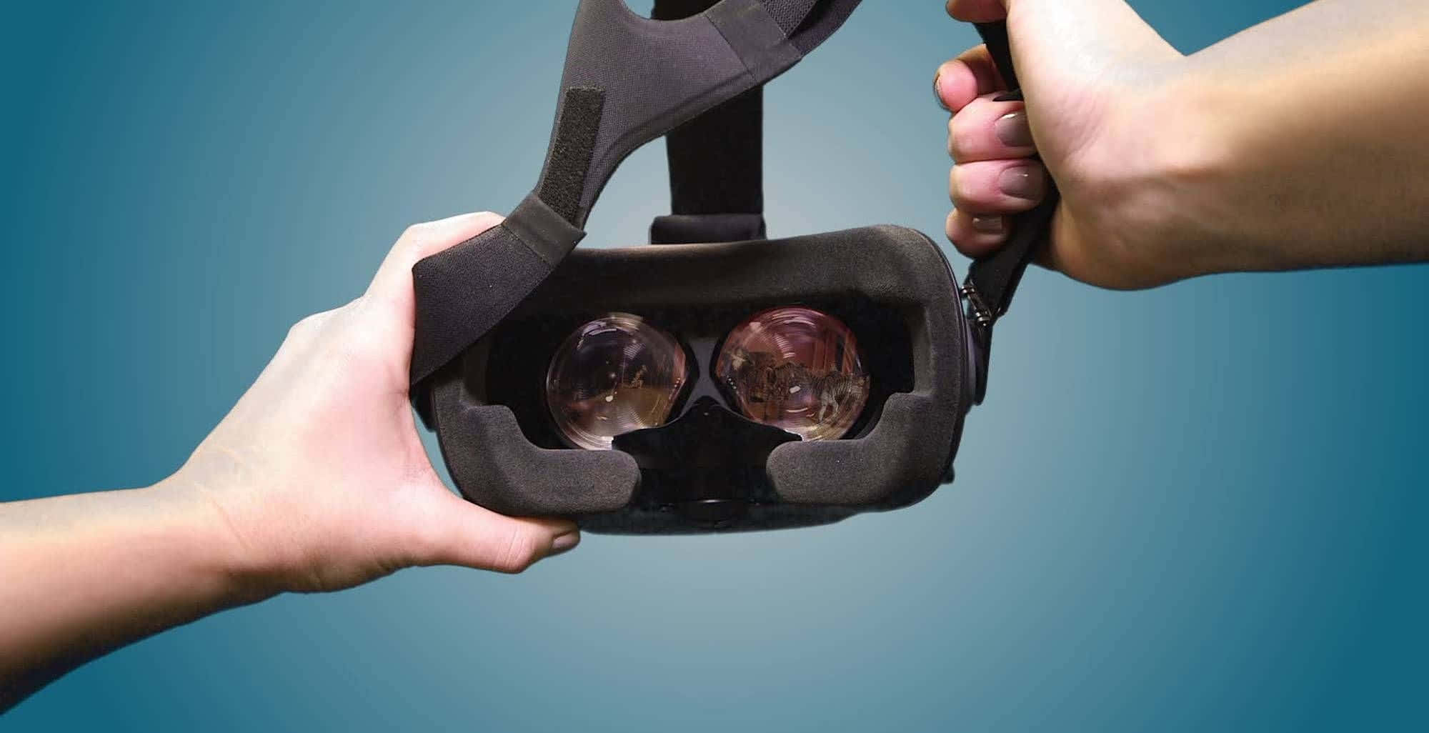 vr 桌布 壁紙 — 兩隻手在漸變藍色背景前握住一個黑色VR頭戴式裝置。