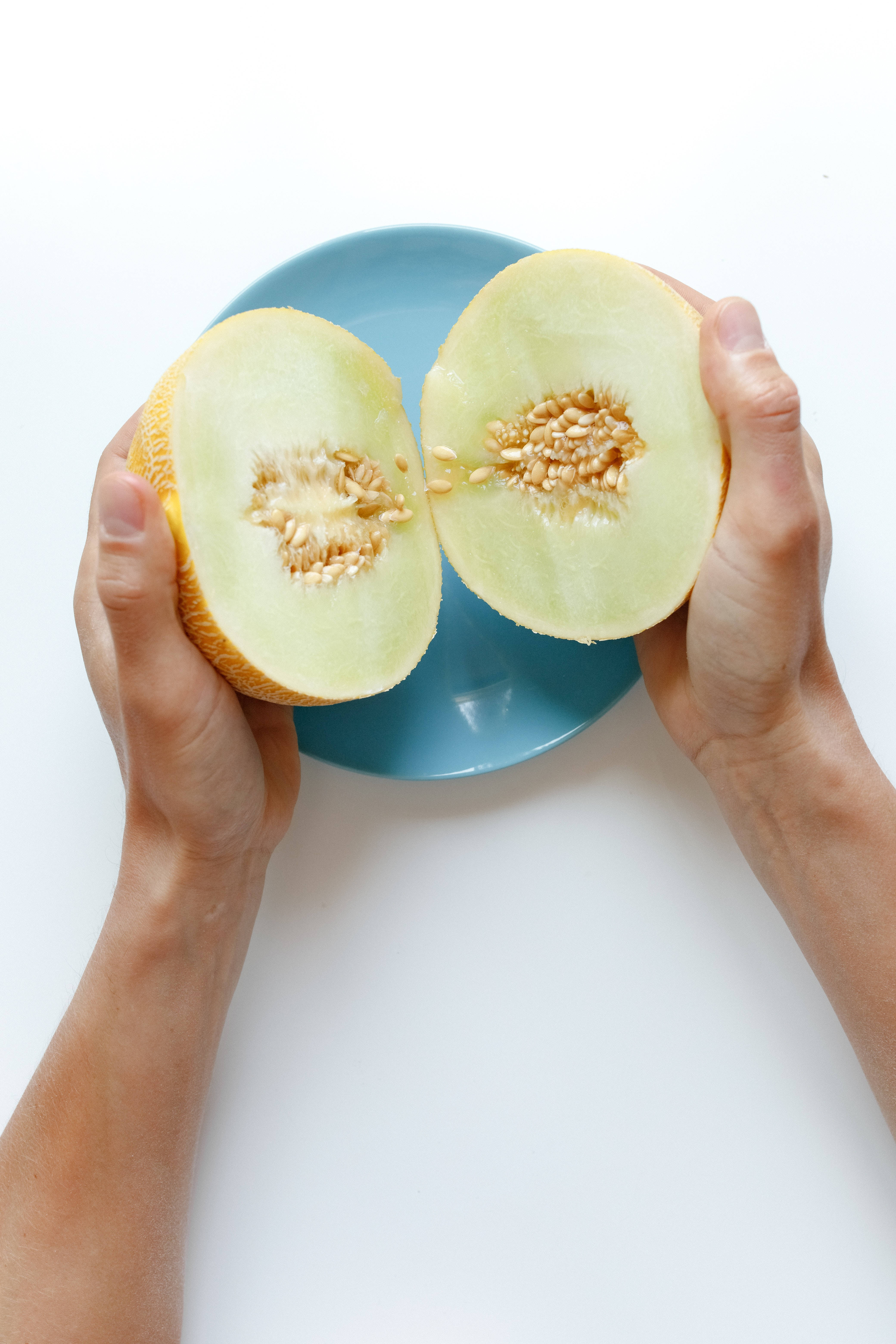 Fruits 桌布 壁紙 — 兩隻手在純白背景上，在藍色盤子上方拿著半個哈密瓜。