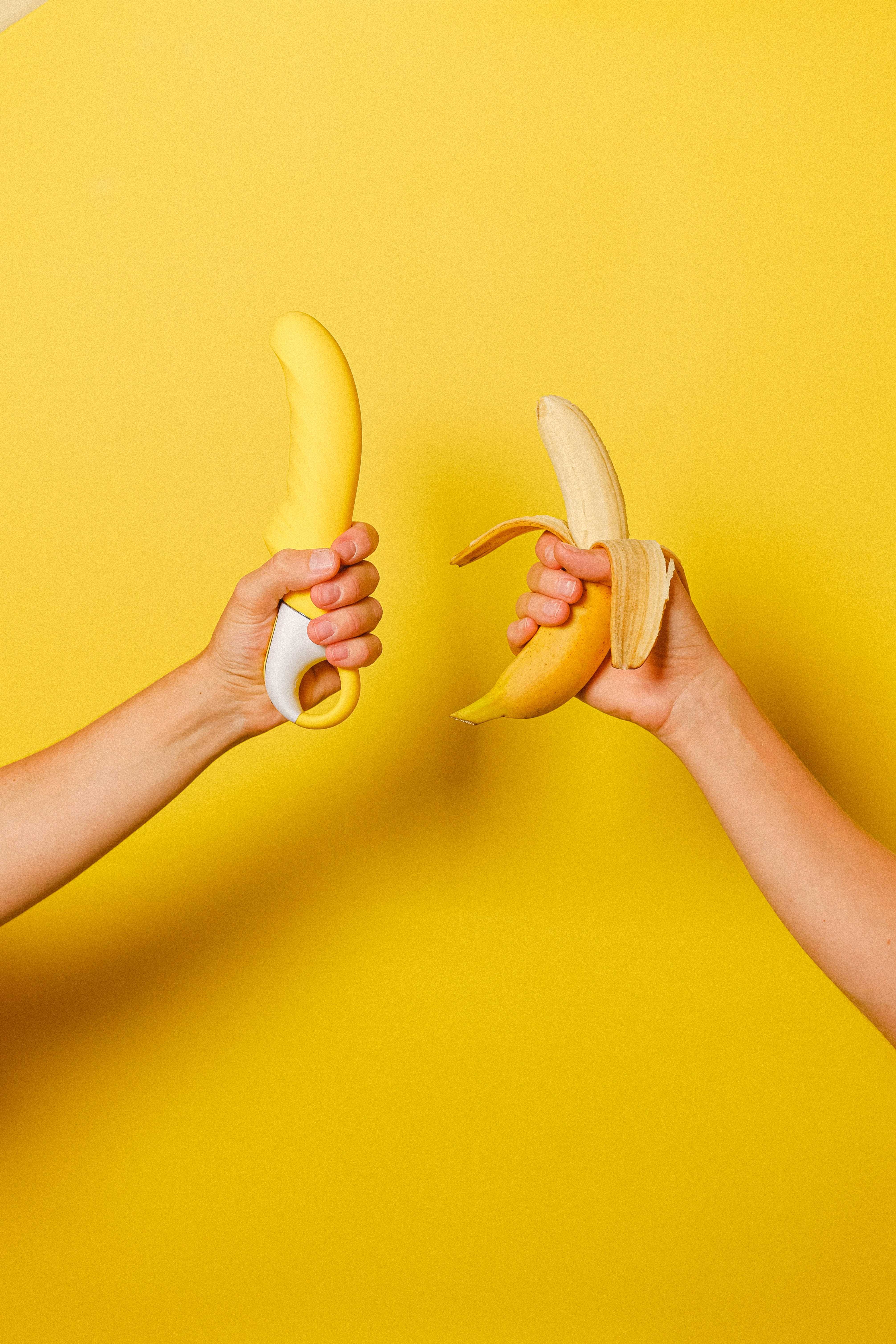 Sexual 桌布 壁紙 — 兩隻手在純黃色背景前拿著一根香蕉和一個香蕉形的按摩棒。