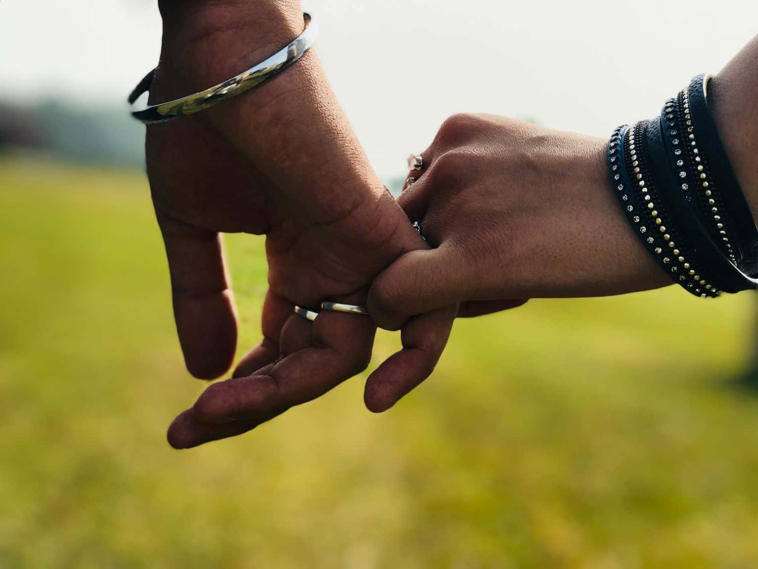 Holding Hands 桌布 壁紙 — 兩隻手在草地上輕輕交握，柔和陽光穿透其間。
