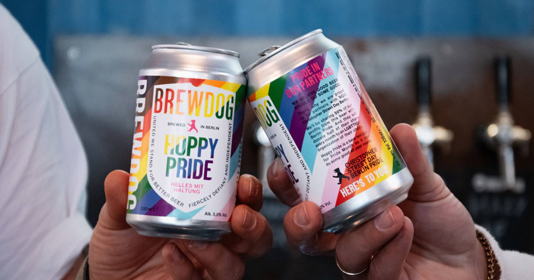 Drink 桌布 壁紙 — 兩隻手在酒吧裡用彩虹主題的BrewDog啤酒罐碰杯，慶祝Pride。