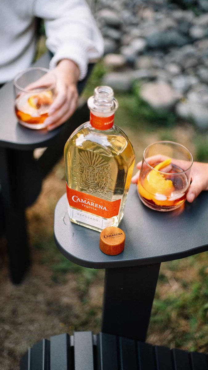 Tequila 桌布 壁紙 — 兩隻手在黑色戶外桌上拿著雞尾酒，旁邊有一瓶Camarena龍舌蘭酒，地面是石頭。