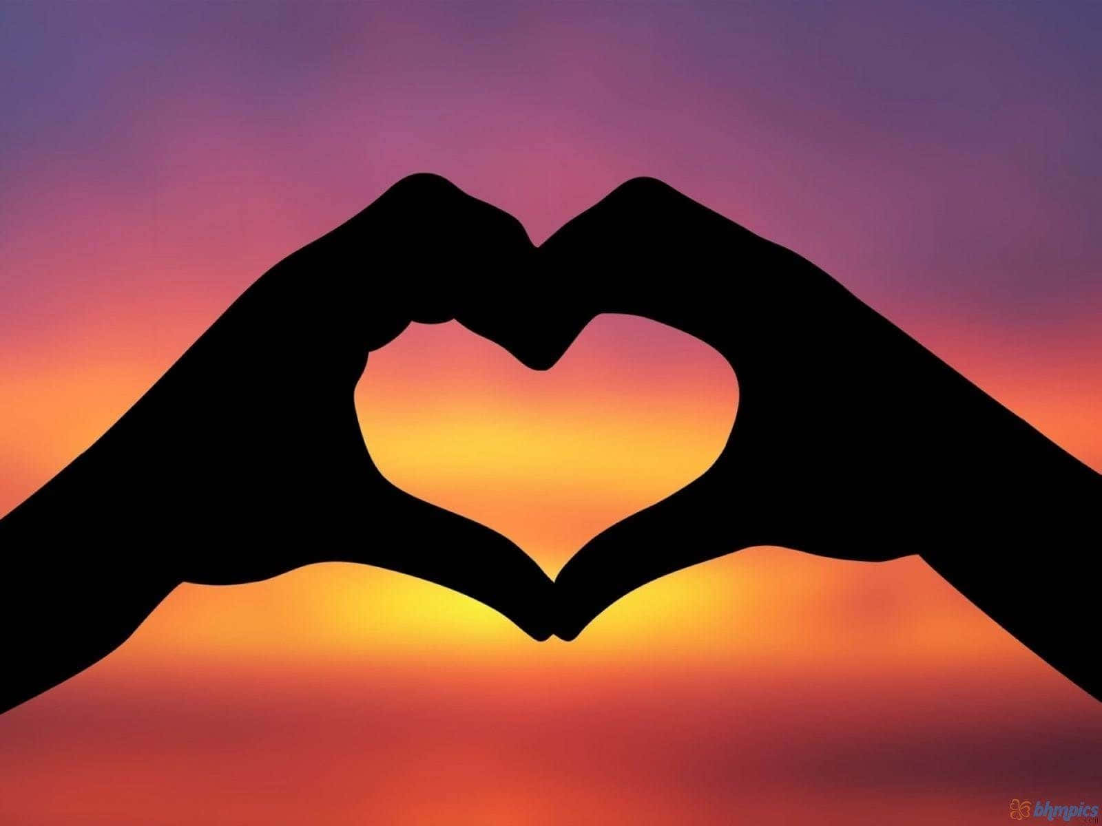 桌布 壁紙 — 兩隻手形成心形剪影，襯托著融合橙色、粉紅色和紫色色調的充滿活力的日落天空。