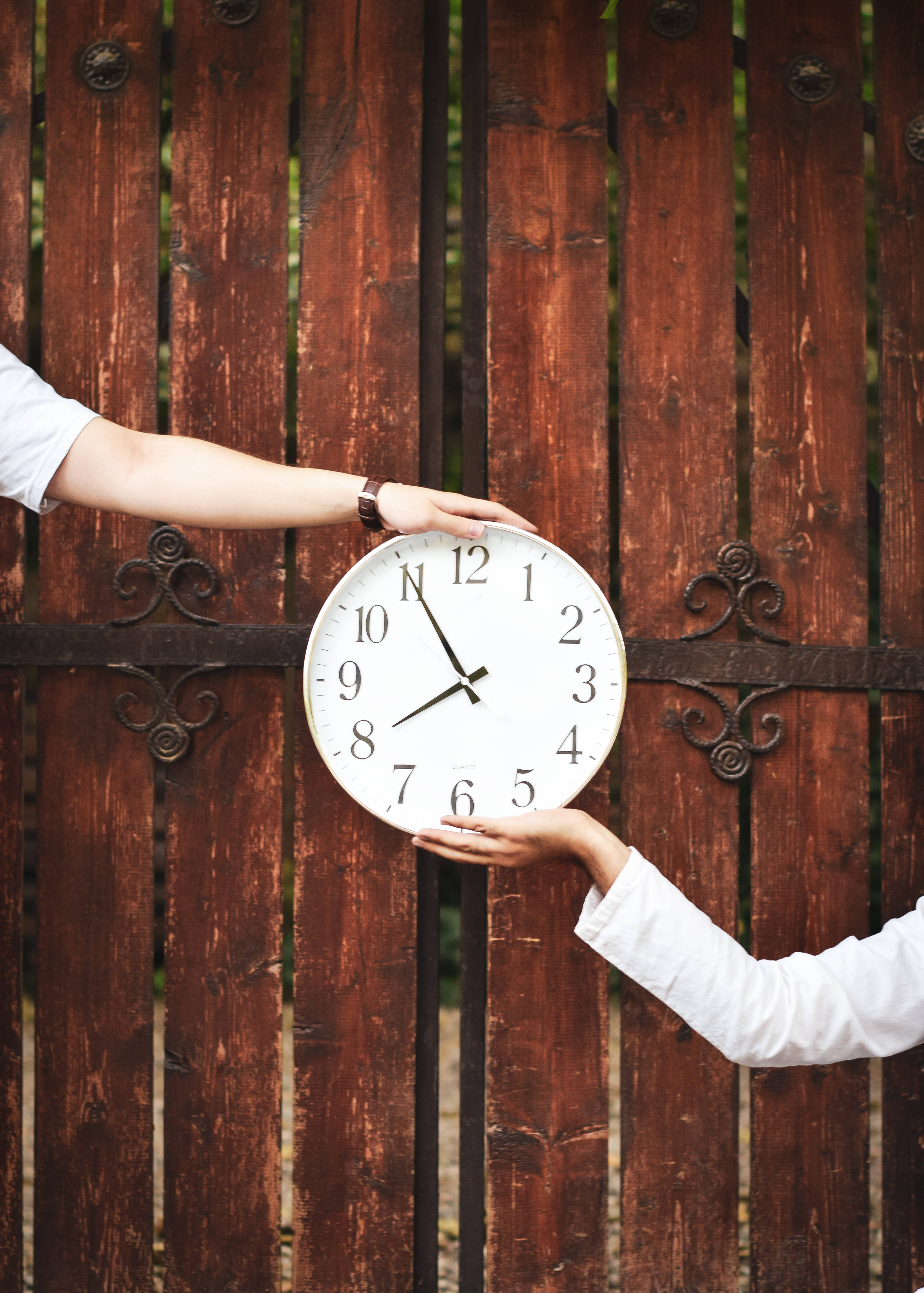 Clock 桌布 壁紙 — 兩隻手拿著一個大型白色指針時鐘，背景是經風化的木柵欄，帶有華麗的金屬工藝。