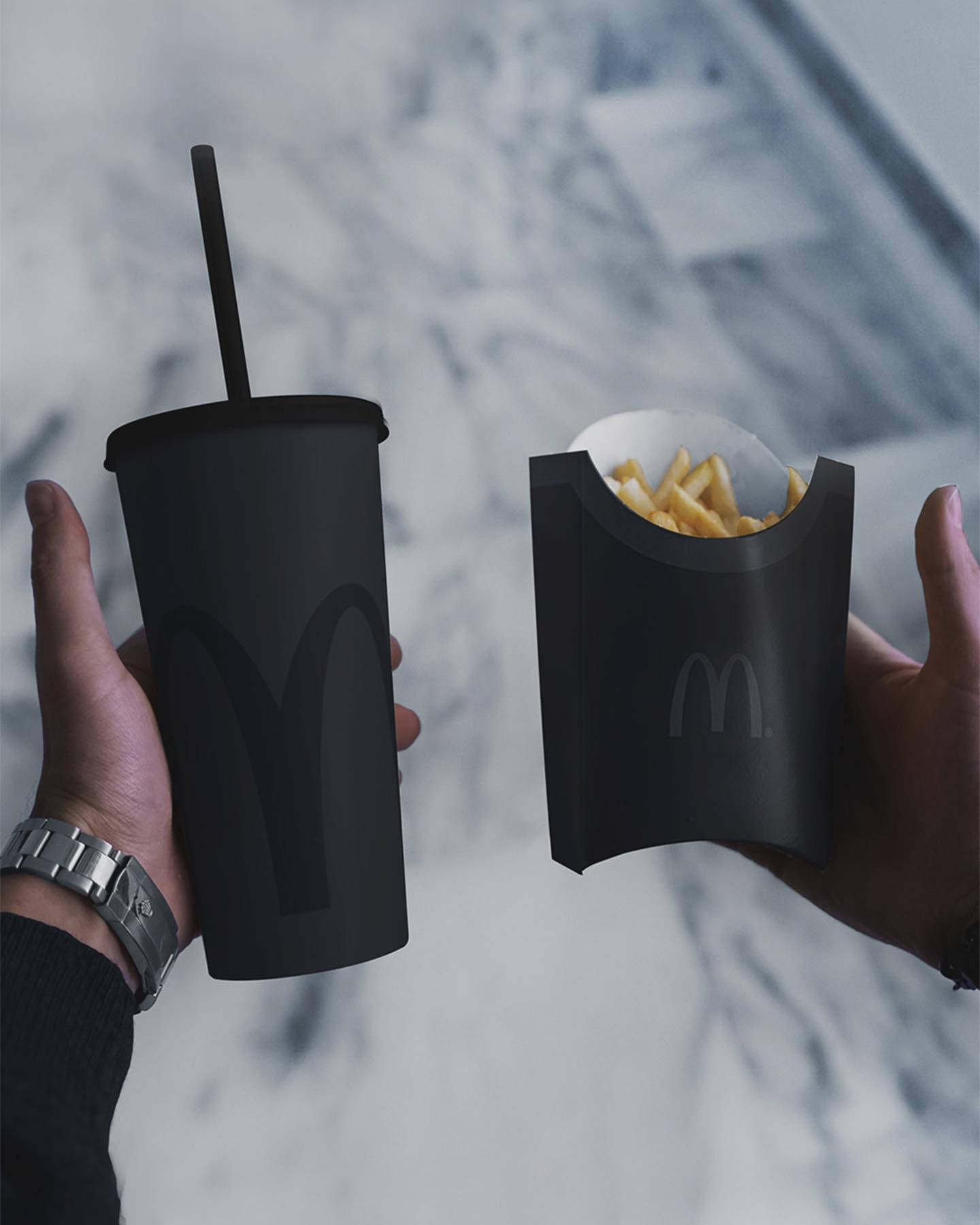 Blvck Paris 桌布 壁紙 — 兩隻手拿著一個霧面黑色的麥當勞飲料杯和薯條盒，背景是模糊的大理石。