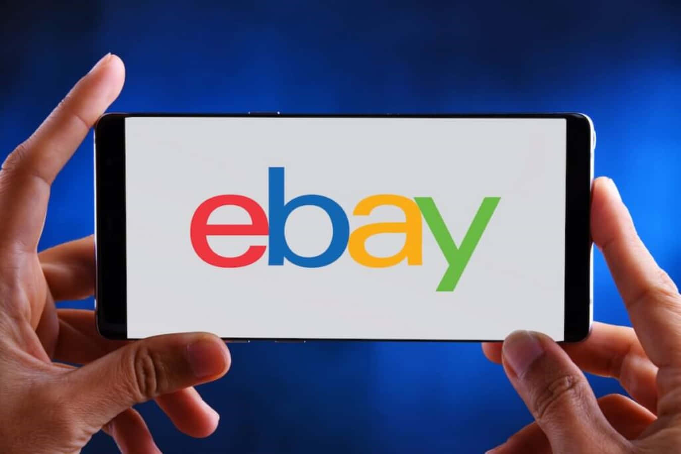 eBay 桌布 壁紙 — 兩隻手拿著一支智慧型手機，在深藍色背景上顯示色彩繽紛的eBay標誌。