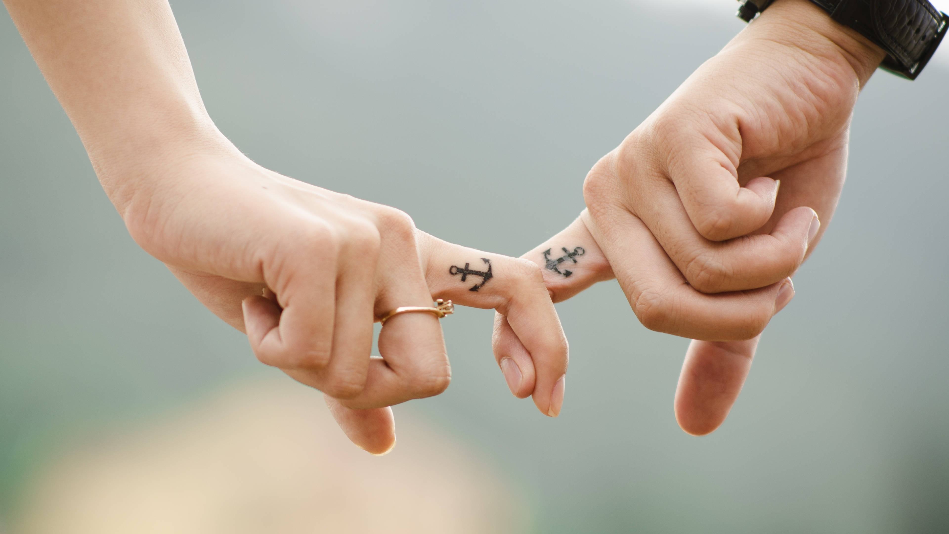 tattoos 桌布 壁紙 — 兩隻手指尖上有匹配的錨紋身的手，輕輕觸碰柔和的模糊自然背景。