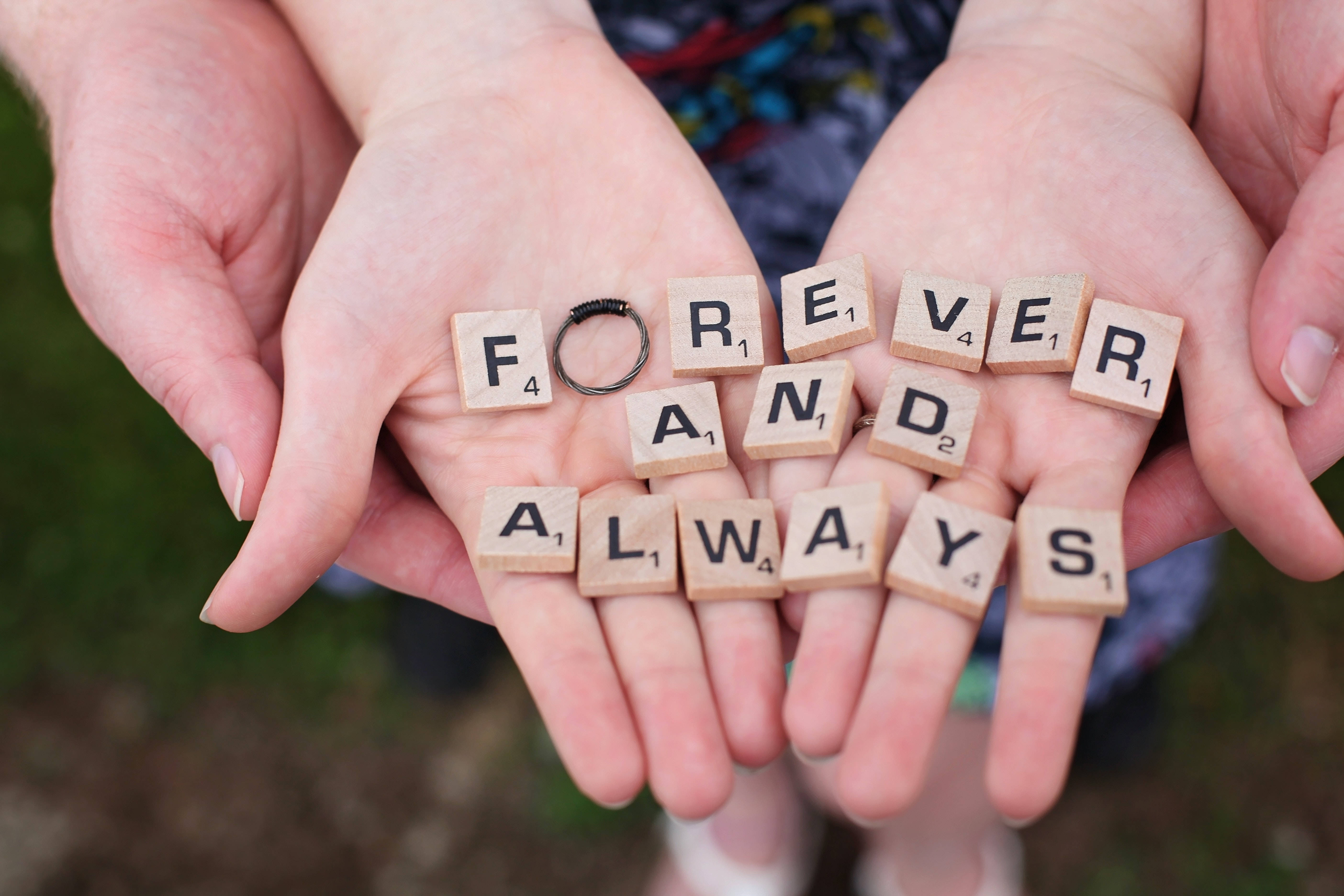 Couple 桌布 壁紙 — 兩隻手捧著木製拼字磚，拼出 forever and always，上面放著一枚結婚戒指。