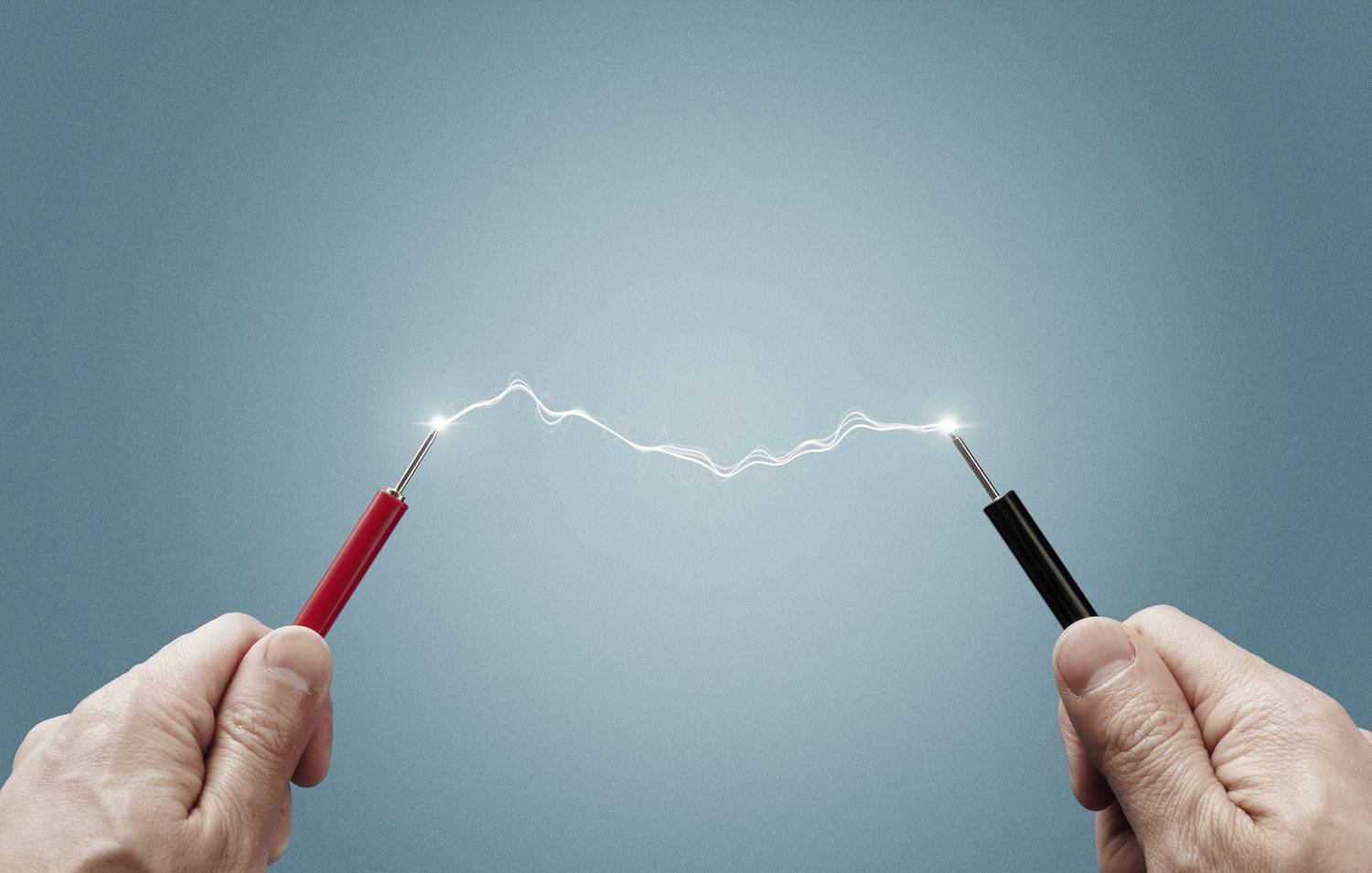 Light 桌布 壁紙 — 兩隻手握住探針，在冷藍色漸變背景上產生明亮的電弧。