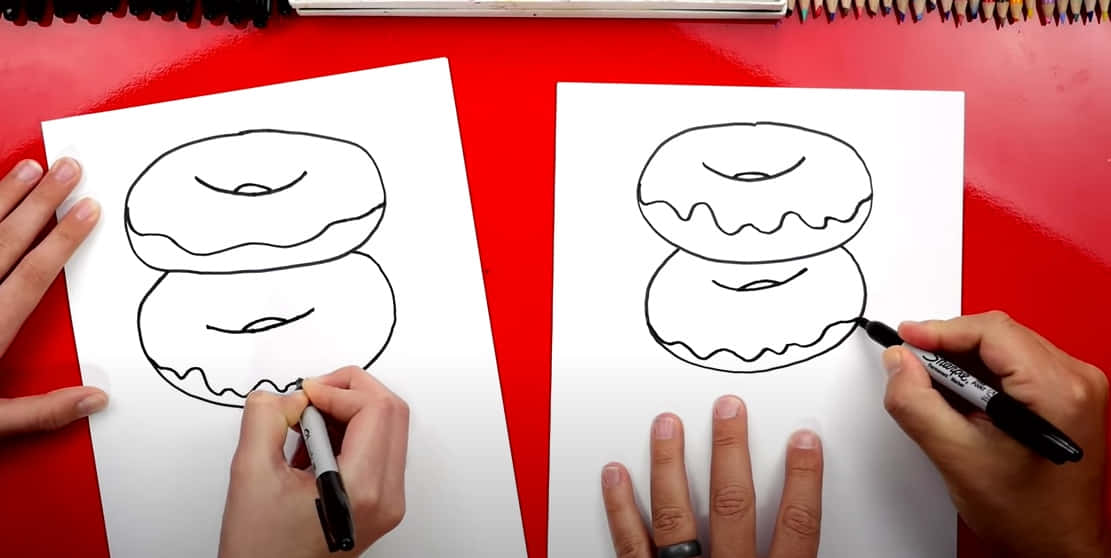 draw 桌布 壁紙 — 兩隻手用黑色馬克筆在白色紙上畫甜甜圈，背景是鮮紅色。