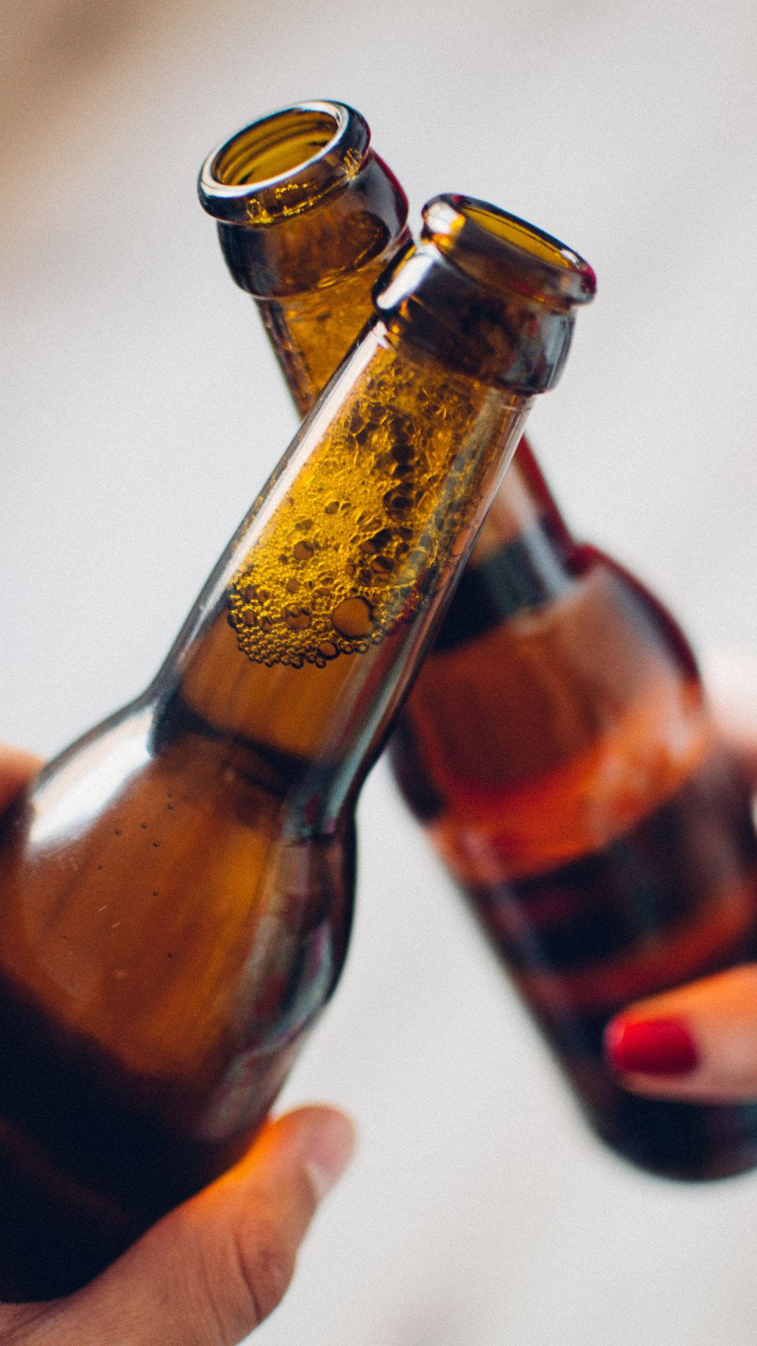 alcohol 桌布 壁紙 — 兩隻手碰撞琥珀色啤酒瓶，金色氣泡升起，近距離乾杯。