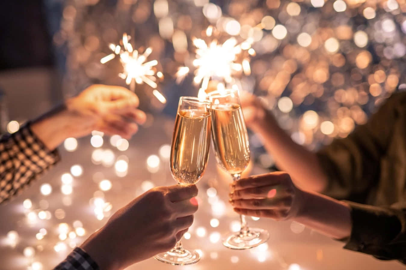 New Years Eve 桌布 壁紙 — 兩隻手碰杯香檳杯，同時仙女棒在閃爍的童話燈光背景下點燃。