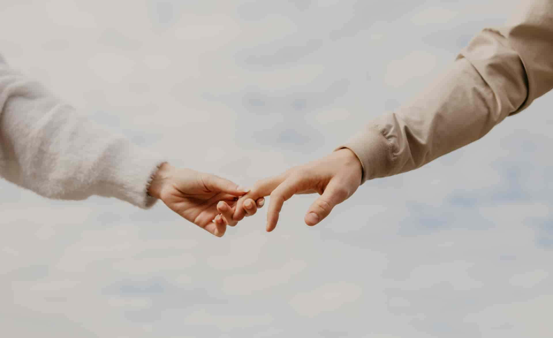 Holding Hands 桌布 壁紙 — 兩隻手穿過多雲的天空，輕輕觸碰指尖，形成一個溫柔的聯繫時刻。