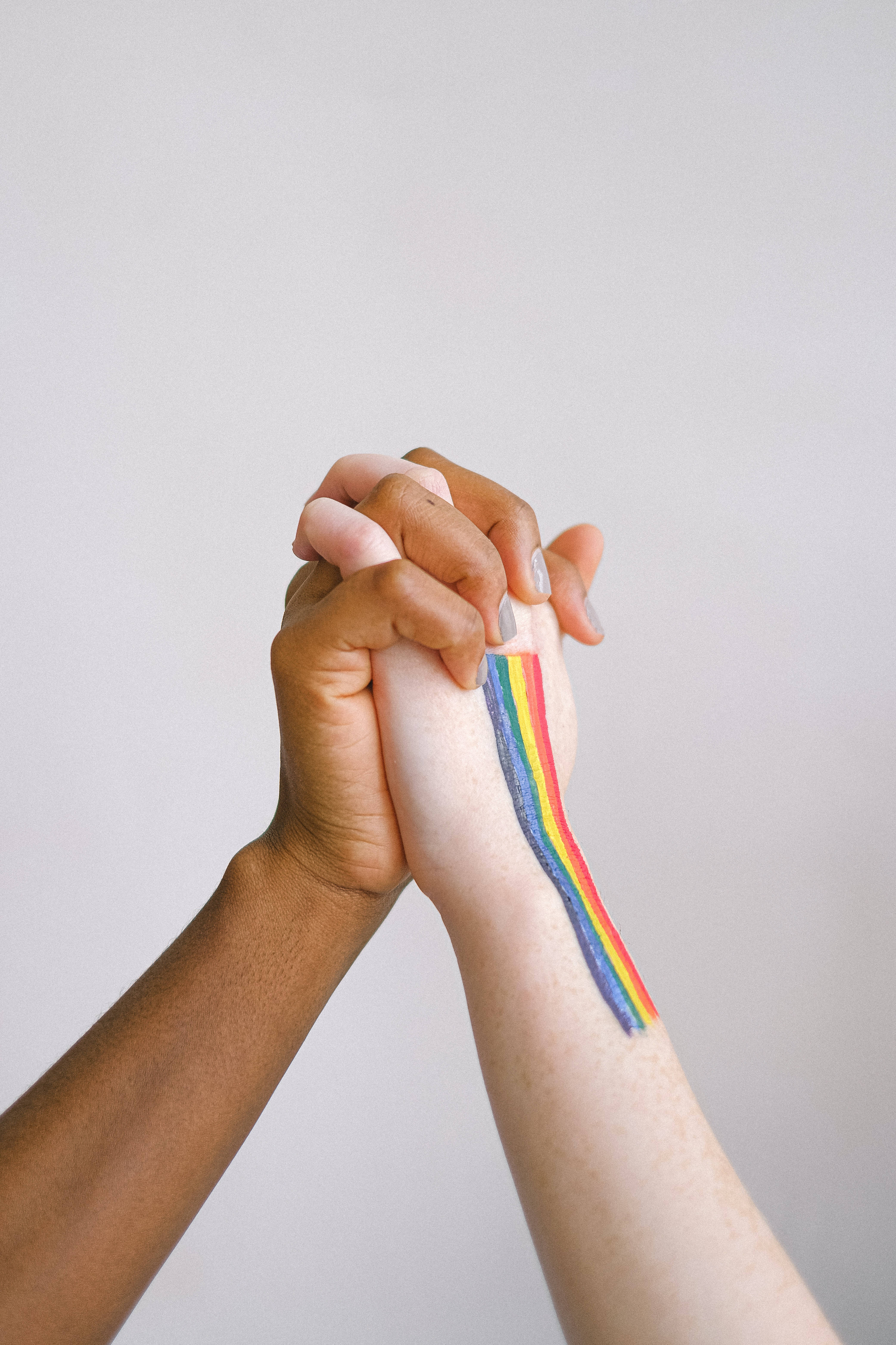 Lesbian Flag 桌布 壁紙 — 兩隻手緊握在一起，其中一隻手腕上纏繞著彩虹旗絲帶，背景為純色。