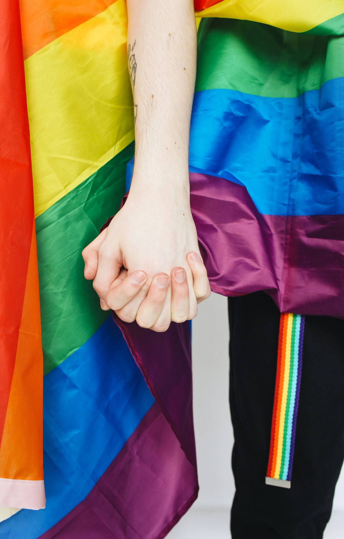 Subtle Lgbt 桌布 壁紙 — 兩隻手緊握在一起，包裹在充滿活力的彩虹旗中，象徵團結與驕傲。