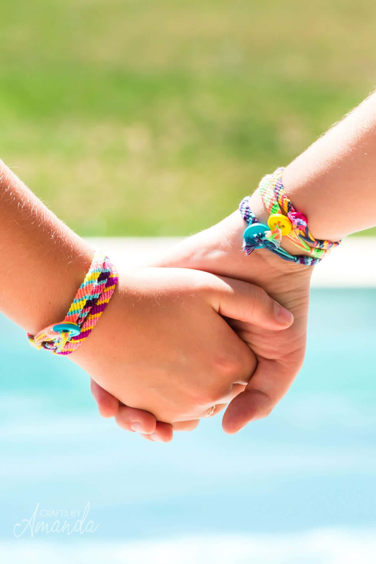 Holding Hands 桌布 壁紙 — 兩隻手緊握在一起，戴著色彩繽紛的友誼手環，背景是模糊的泳池邊。