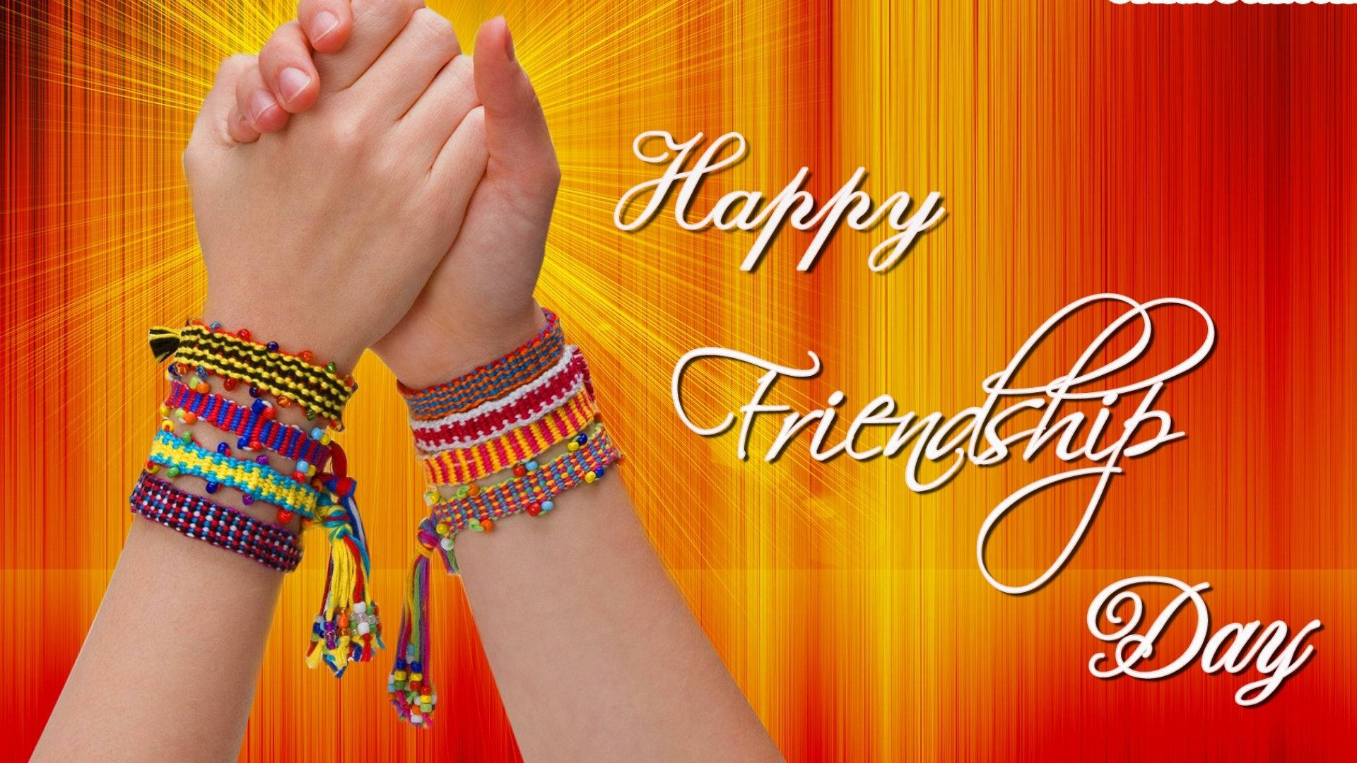 Friendship Day 桌布 壁紙 — 兩隻手緊握在一起，飾以色彩繽紛的友誼手環，背景是明亮的橙黃漸層色，並帶有慶祝文字。