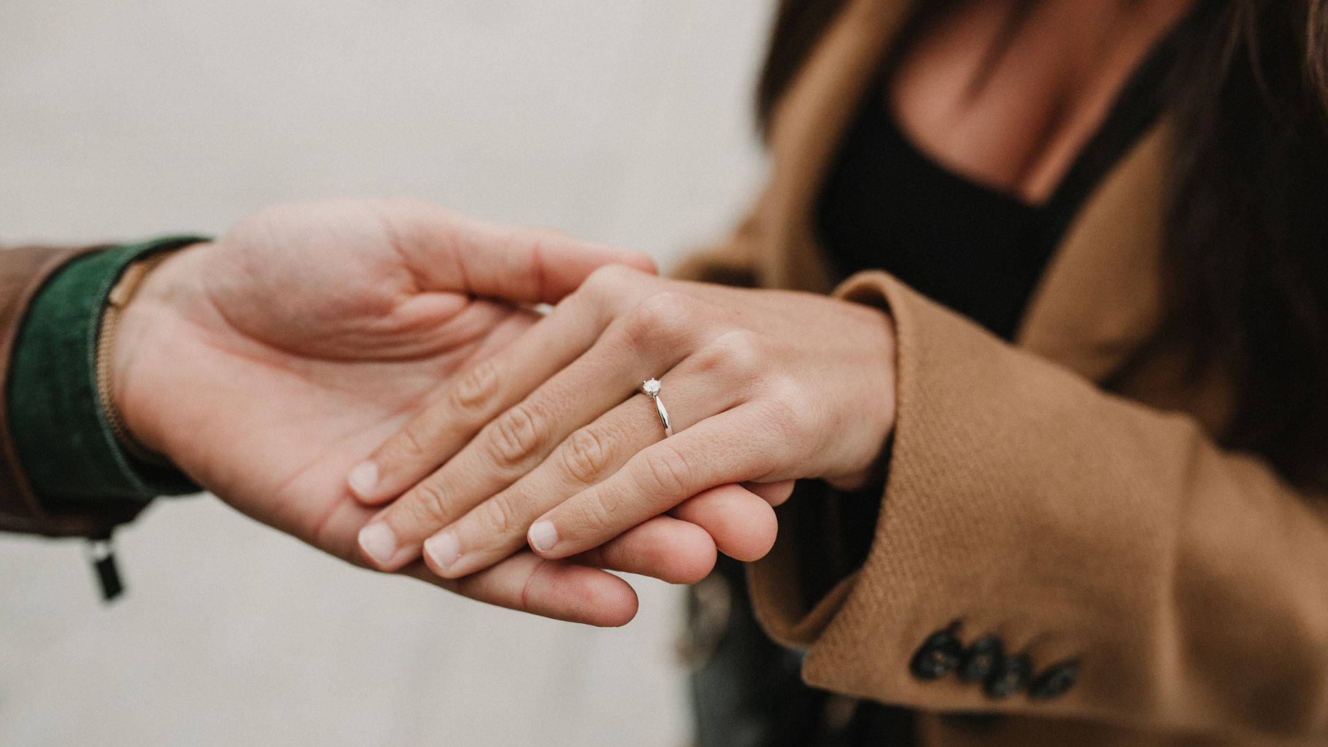 Wedding Rings 桌布 壁紙 — 兩隻手緊握的特寫，女士手指上戴著閃閃發光的訂婚戒指。