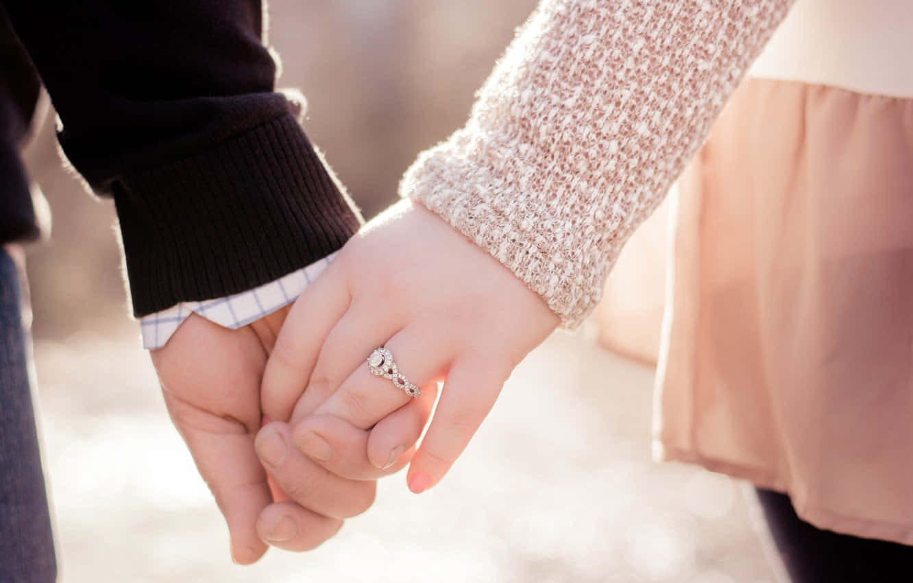 Holding Hands 桌布 壁紙 — 兩隻手緊握的特寫，左手戴著閃閃發光的訂婚戒指，背景柔和模糊。