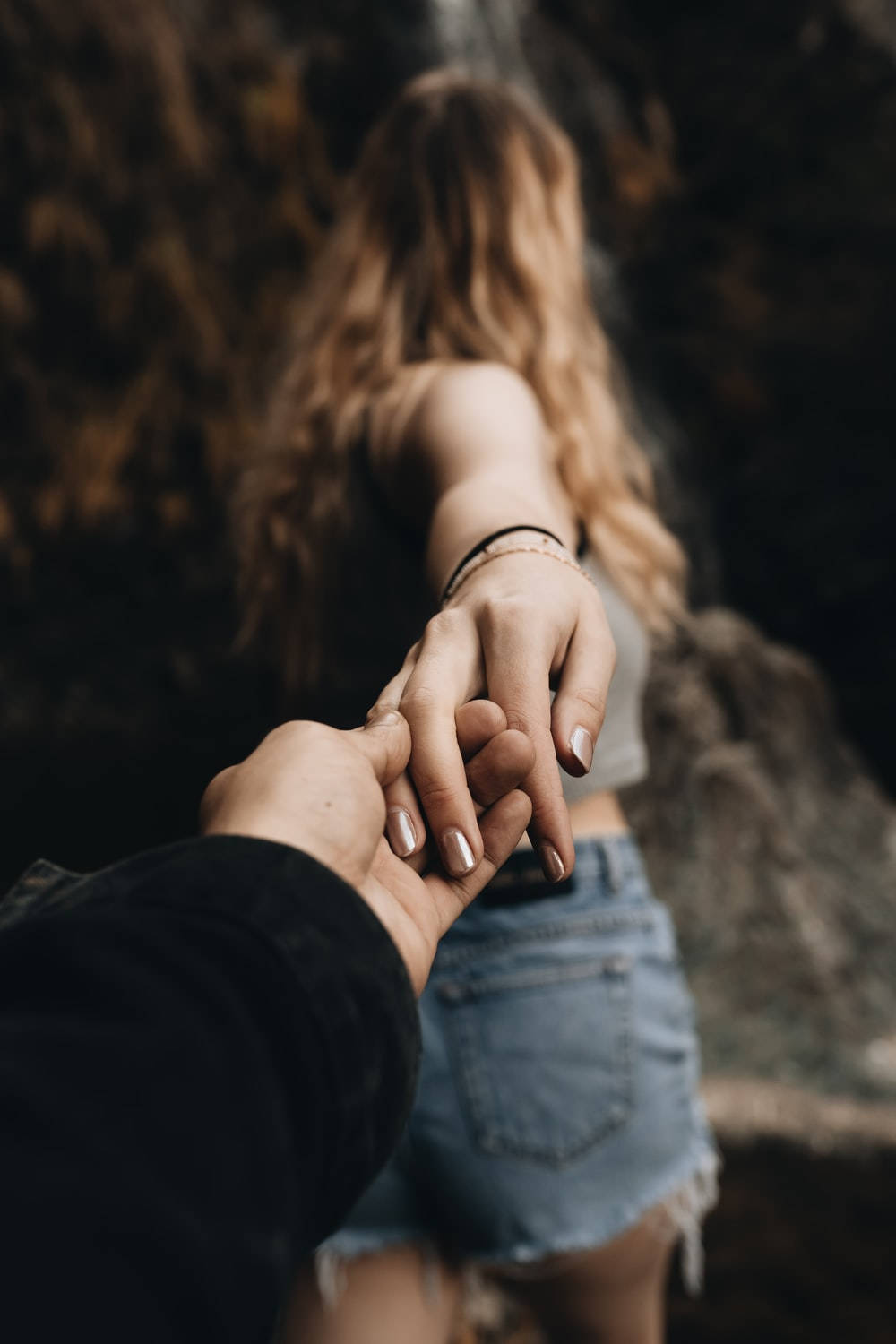 hands 桌布 壁紙 — 兩隻手緊握的特寫，背後是瀑布傾瀉而下，一位身穿牛仔短褲的女性。