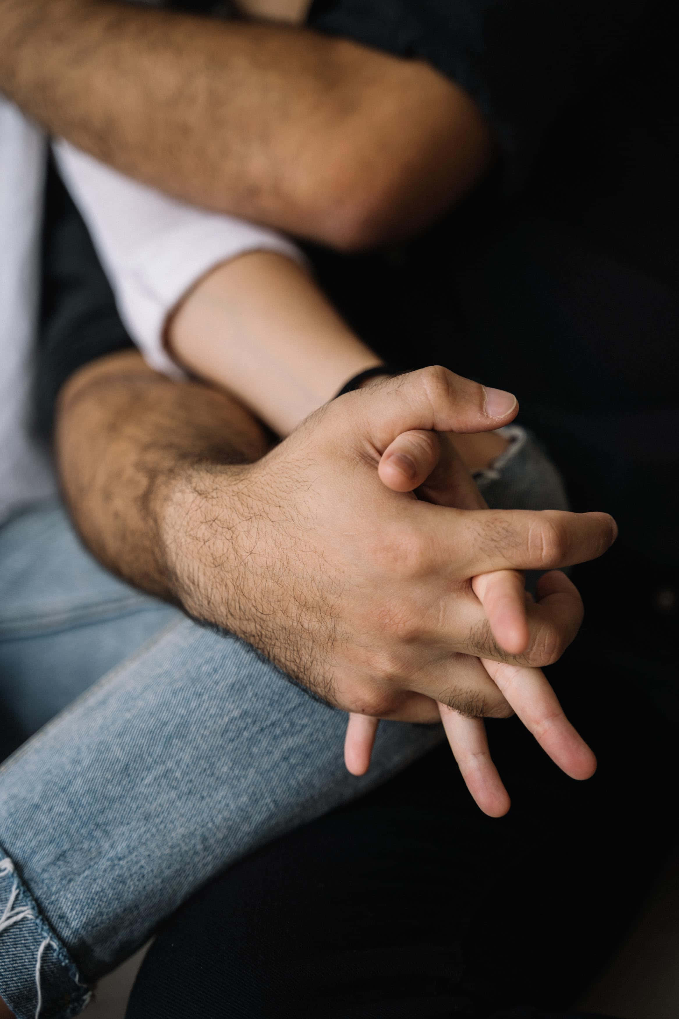 Holding Hands 桌布 壁紙 — 兩隻手緊握的親密特寫，一隻手腕有深色毛髮，另一隻手有淺色皮膚和牛仔褲。