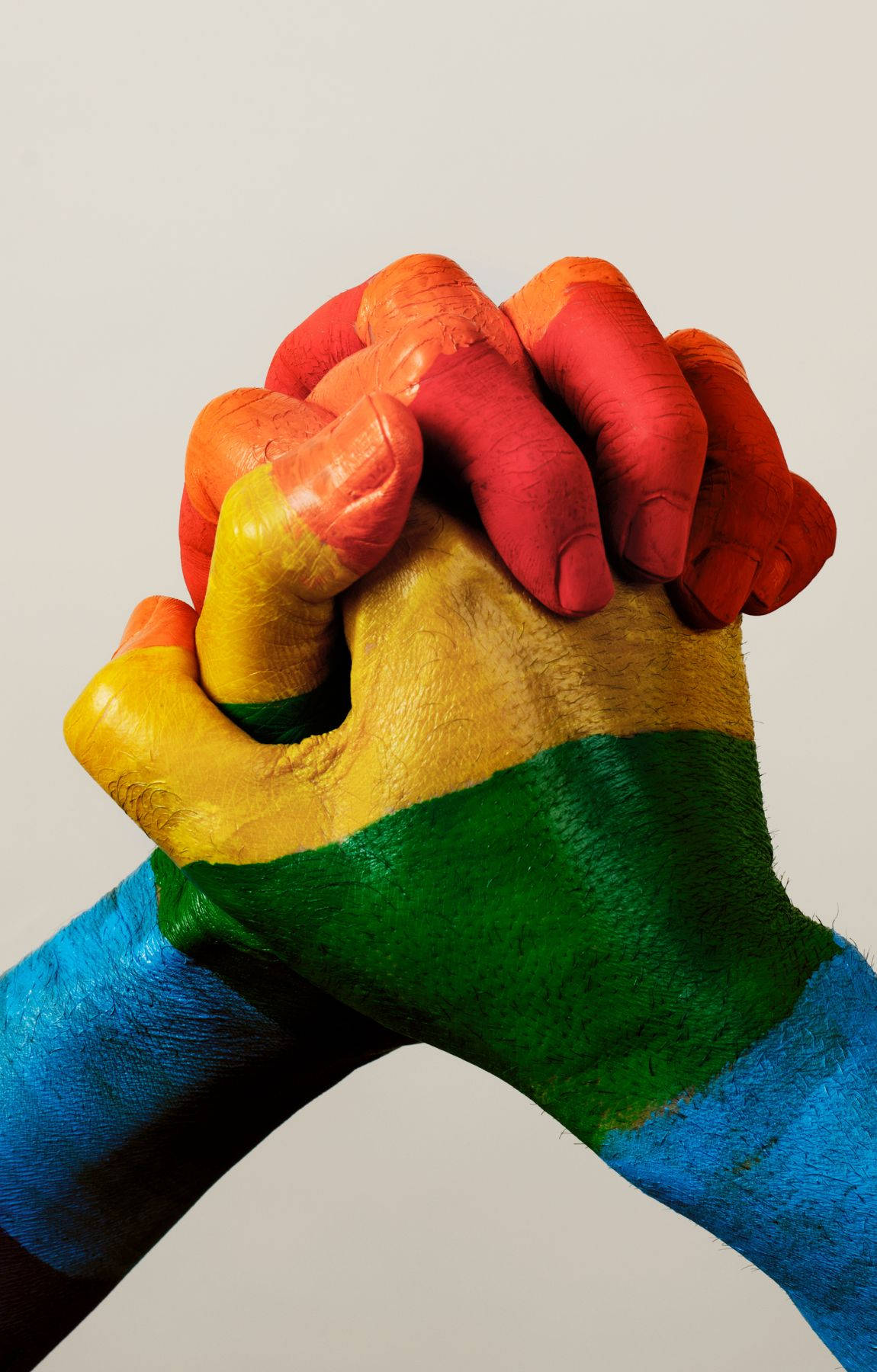 Subtle Lgbt 桌布 壁紙 — 兩隻手緊緊握在一起，以鮮豔的彩虹色彩繪在素色背景上。