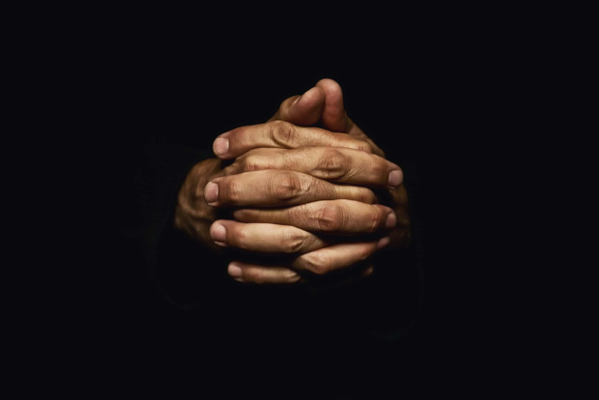 Praying 桌布 壁紙 — 兩隻手緊緊握在一起，做出祈禱或深思的姿勢，背景是純黑色。
