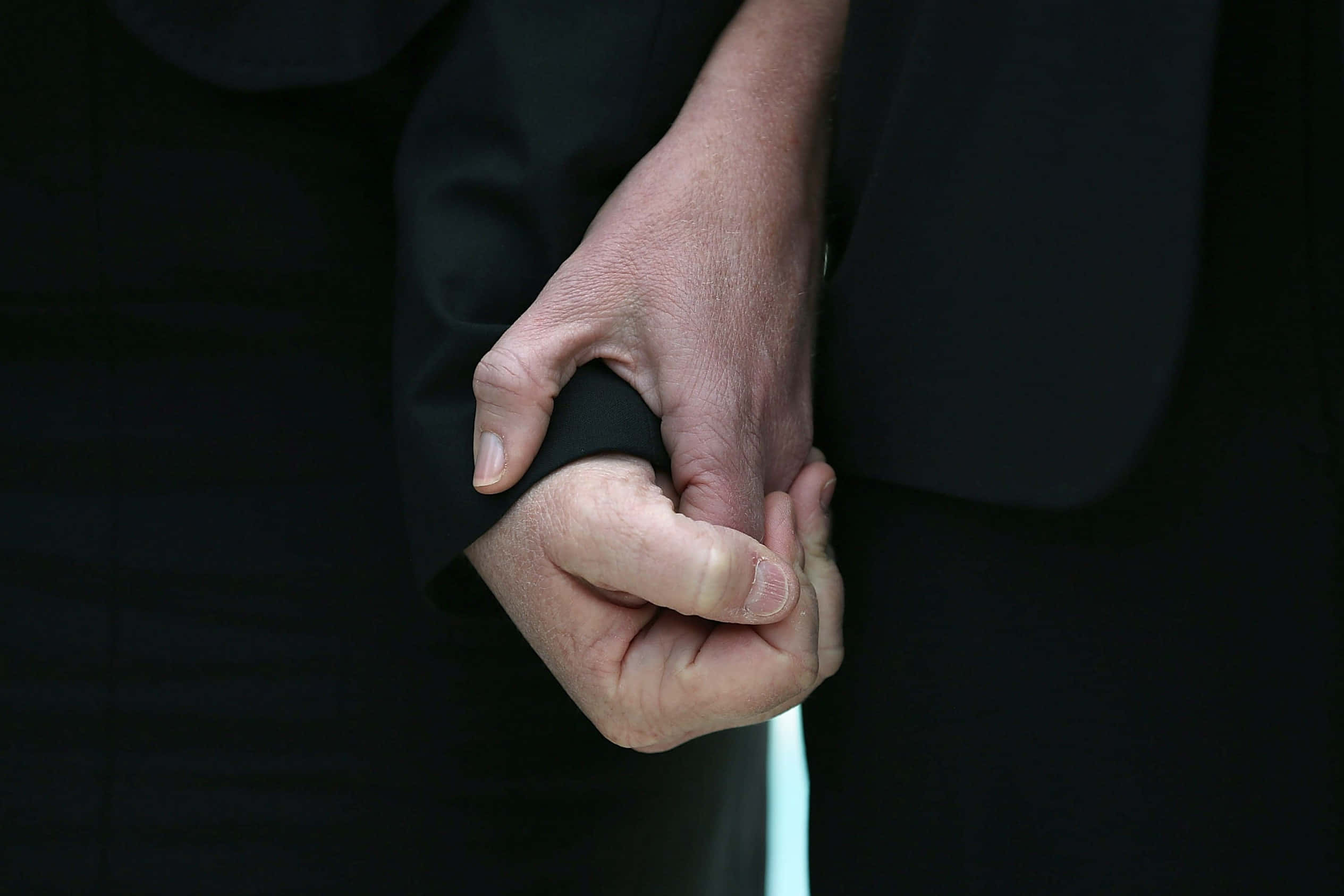 Holding Hands 桌布 壁紙 — 兩隻手緊緊握在深色西裝袖中，傳達深刻的情感支持和親密感。