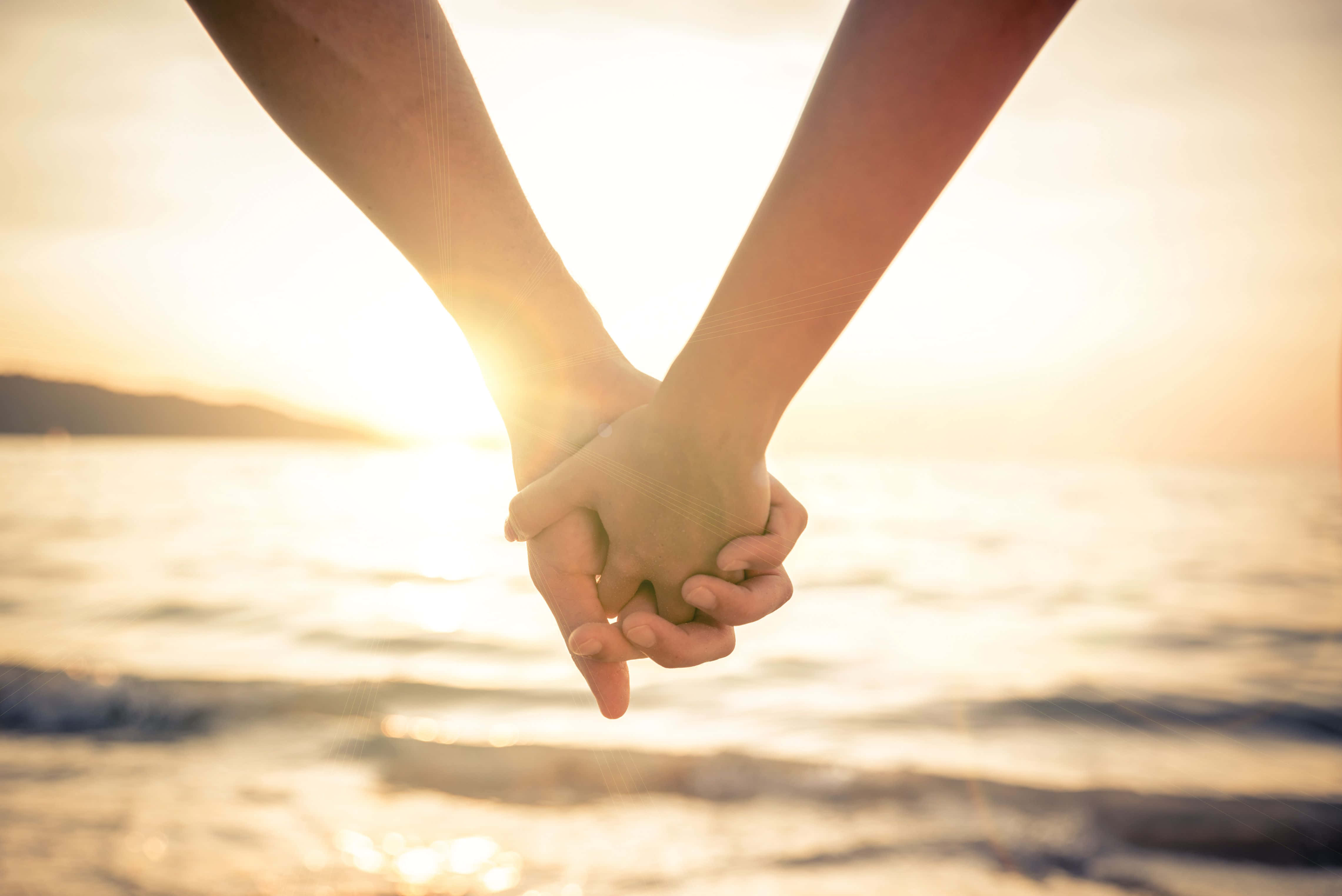couple love 桌布 壁紙 — 兩隻手緊緊相握，映襯著海洋波浪上閃耀的日落。