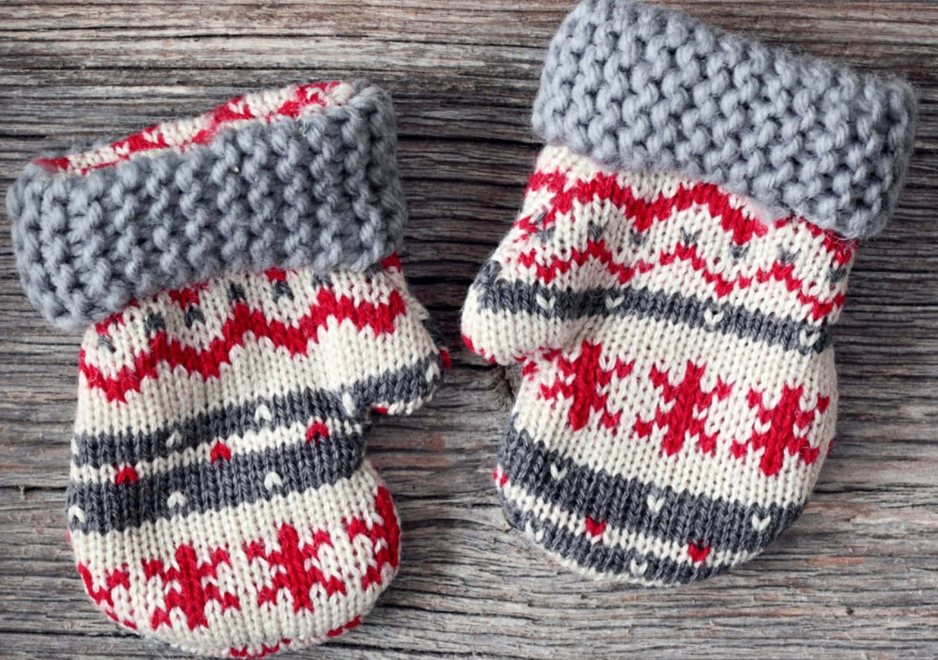 Mittens 桌布 壁紙 — 兩隻手織手套，帶有紅色、灰色和奶油色圖案，放在一塊風化的木質表面上。
