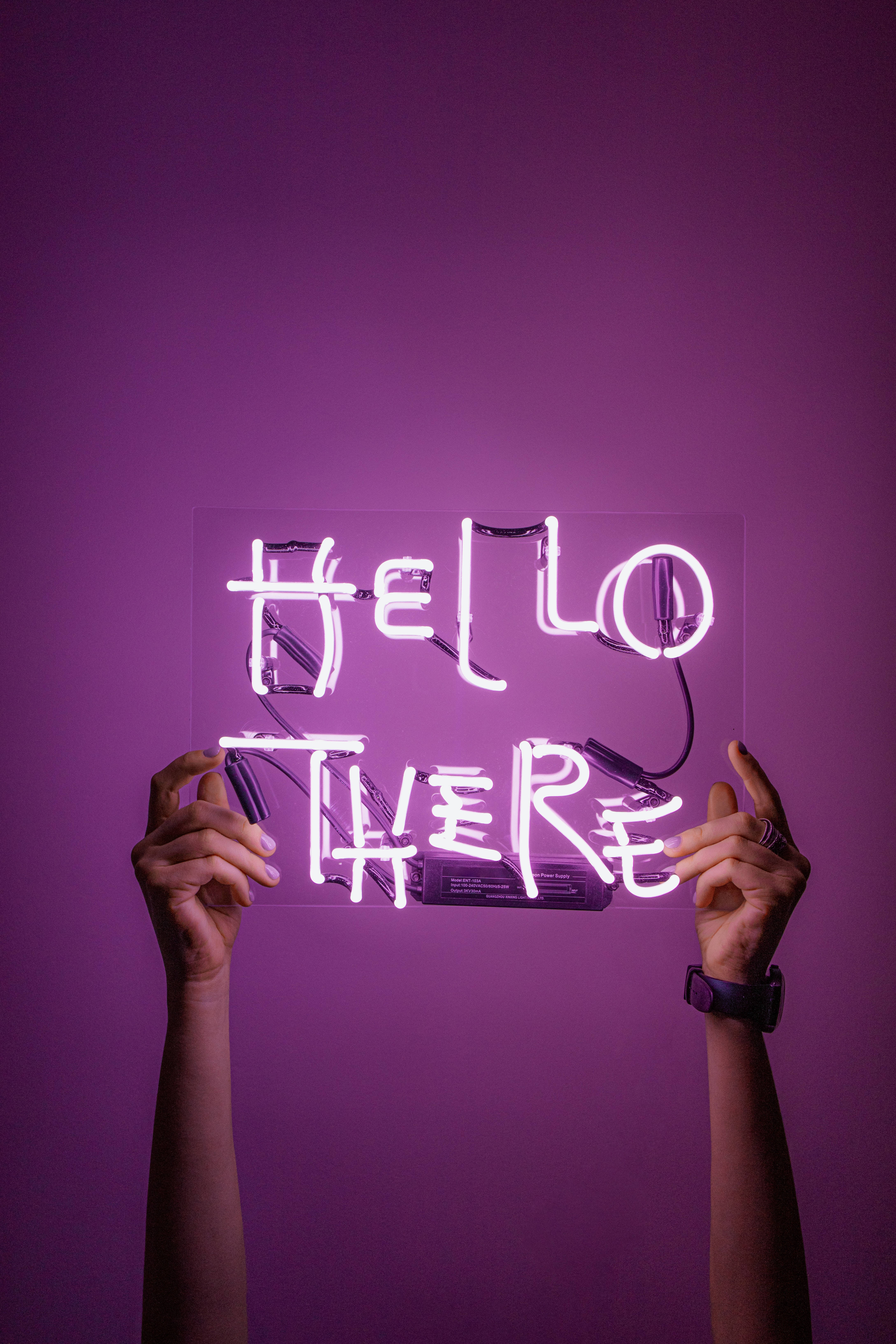 WhatsApp 桌布 壁紙 — 兩隻手舉著一個發光的紫色霓虹燈牌，上面寫著 hello there，背景是純紫色牆壁。
