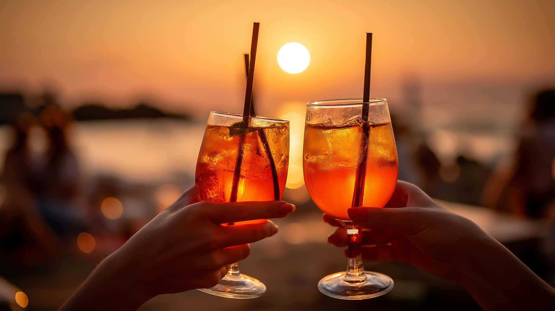 Cheers to Sunset: Aperol Spritz Toast by the Water 壁紙 — 兩隻手舉起冰凍橙汁飲料的玻璃杯，在水面上閃耀的夕陽背景下碰杯。