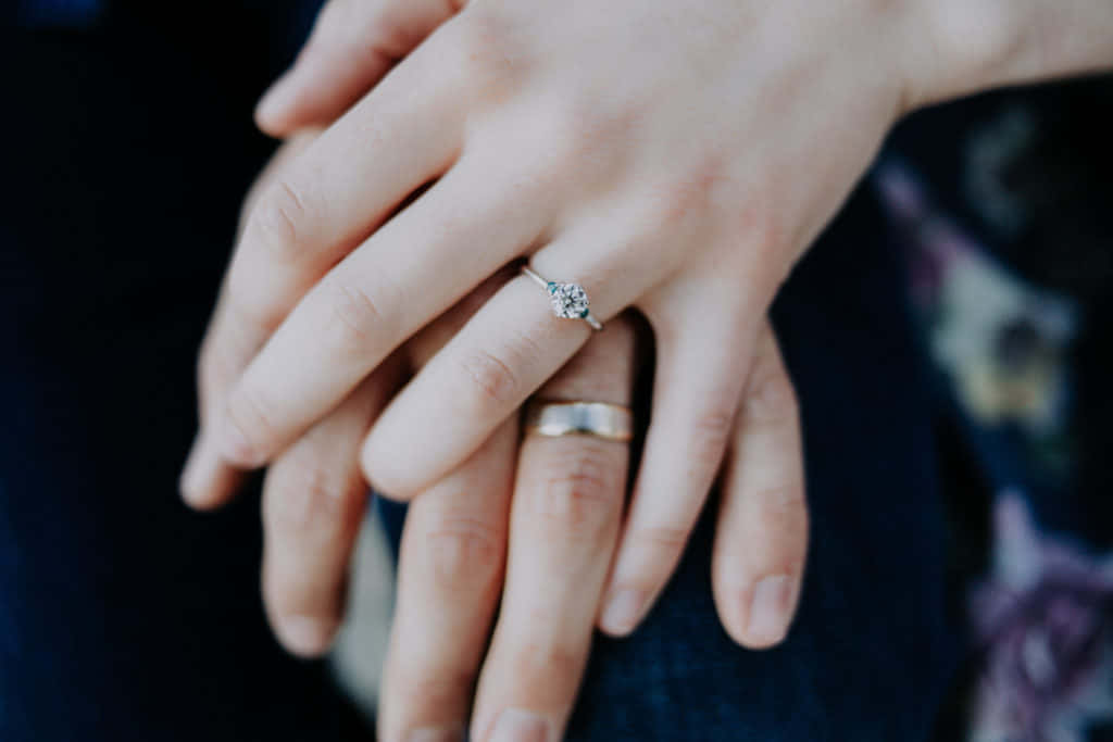 Marriage 桌布 壁紙 — 兩隻手輕輕交握，一隻戴著訂婚戒指，另一隻戴著結婚戒指，在柔和自然光下。