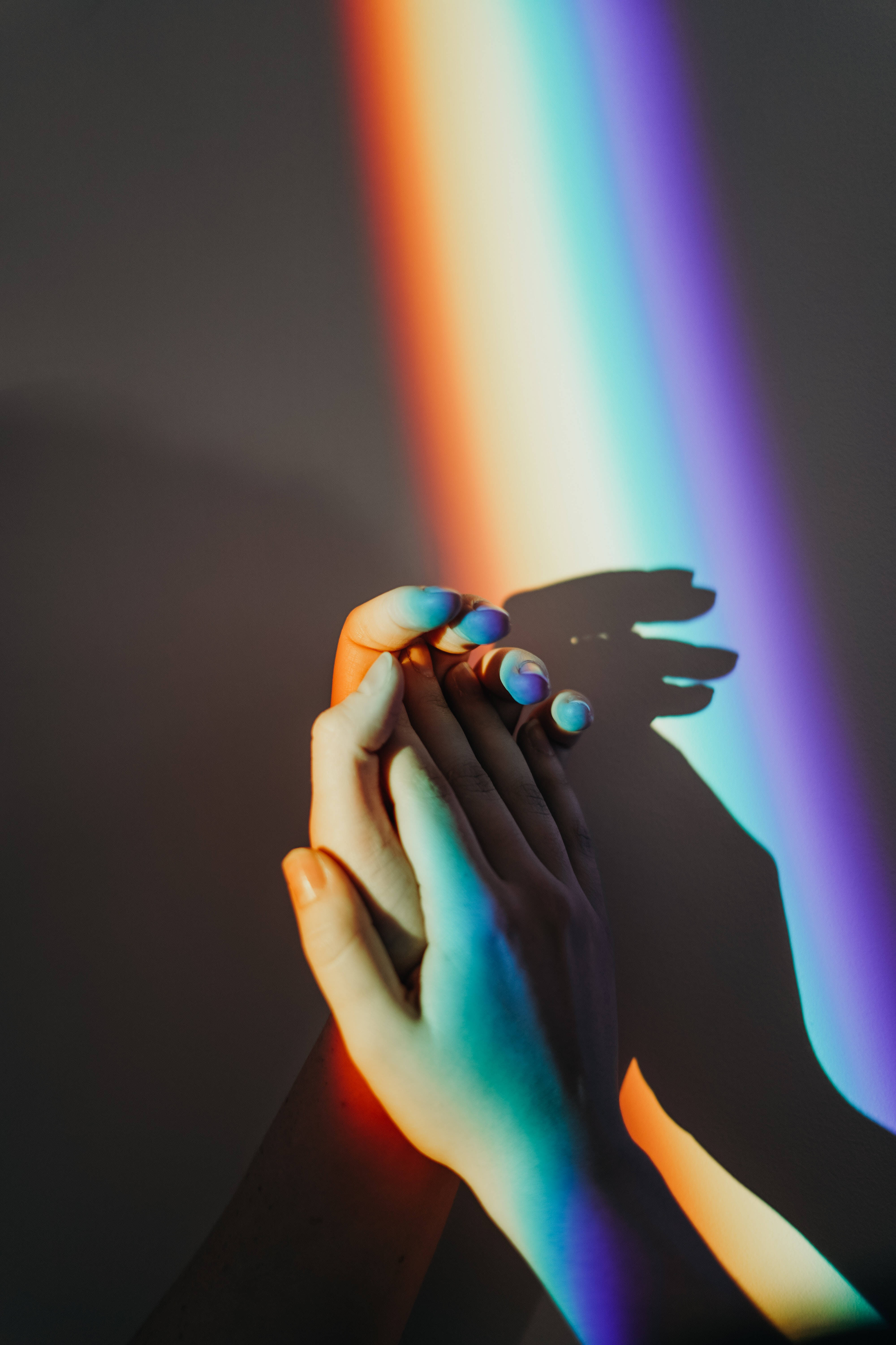 Couple Hands 桌布 壁紙 — 兩隻手輕輕交握，沐浴在鮮豔的彩虹光束中，背景為深色。