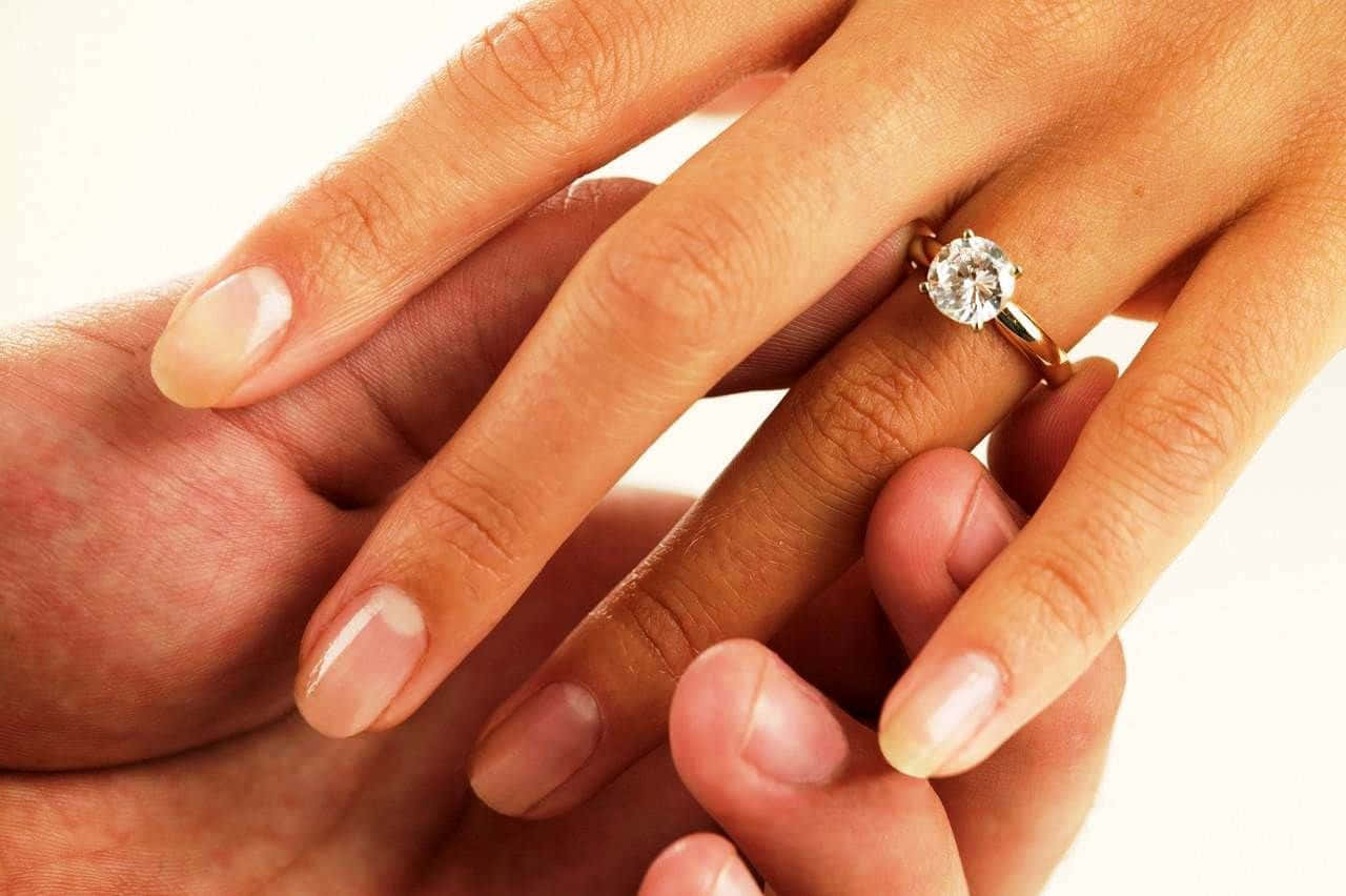 rings 桌布 壁紙 — 兩隻手輕輕交握，無名指上戴著一枚閃閃發光的鑽石訂婚戒指。